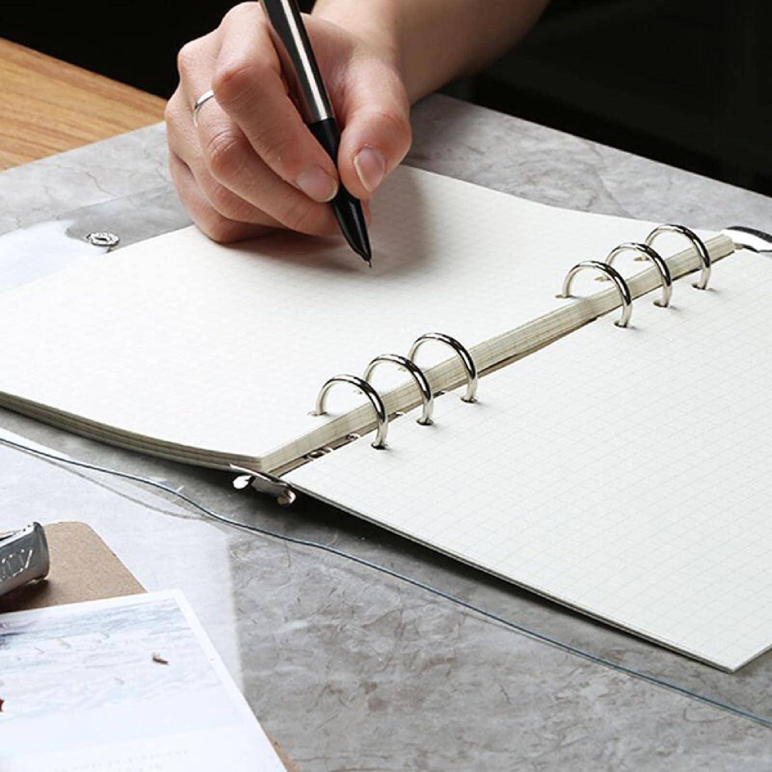 Eine Person, die einen Stift hält, schreibt in einem offenen Spiralblock auf einem Schreibtisch.