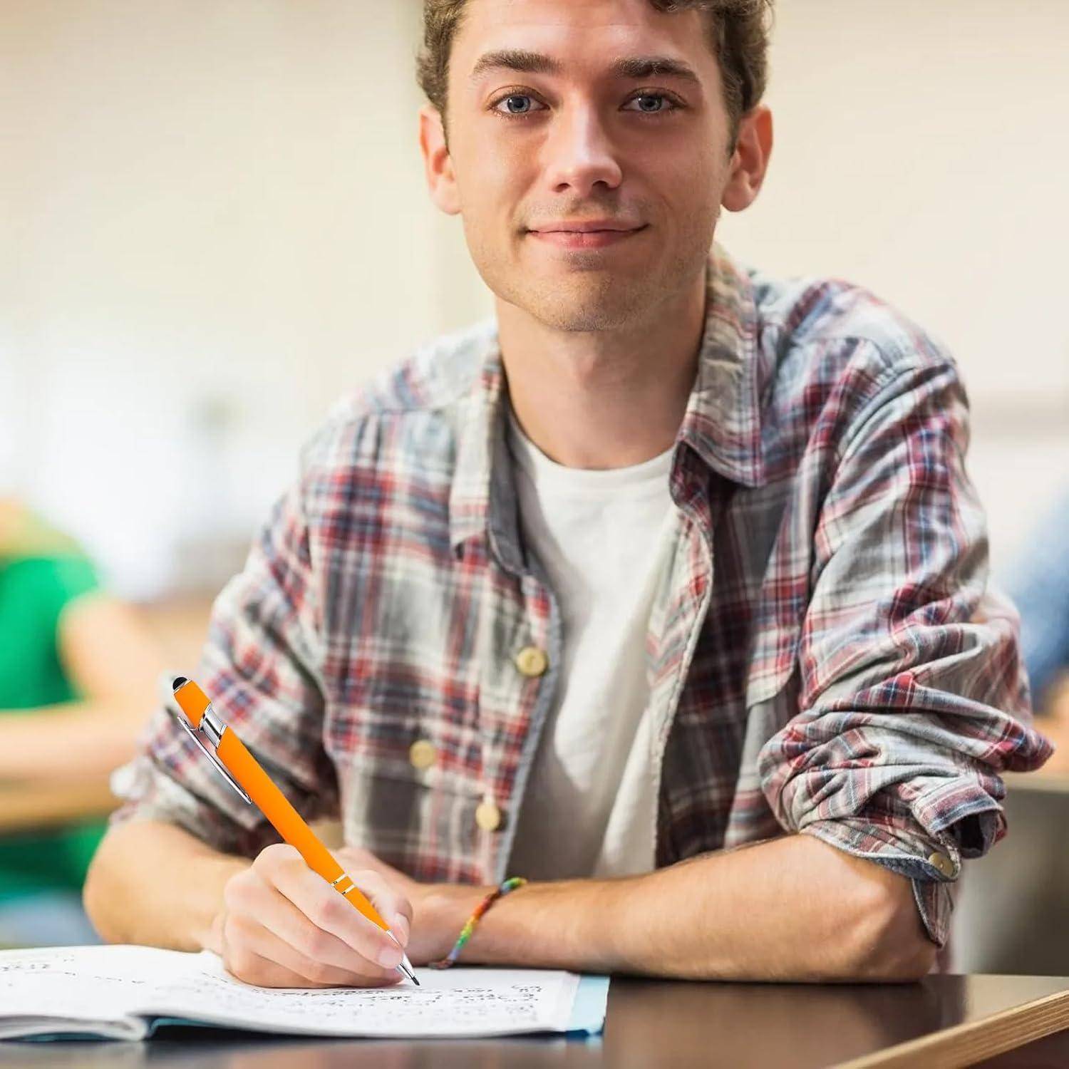 Junger Mann, der an einem Schreibtisch in einem Klassenzimmer oder Lernbereich ein Notizbuch beschreibt und einen orangefarbenen Bleistift hält.