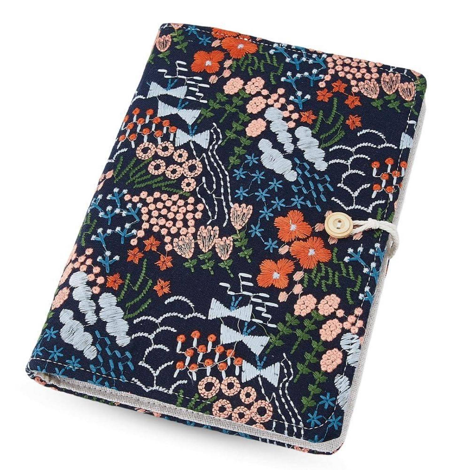 Notizbucheinband aus marineblauem Stoff mit floralen Stickereien und Knopf-und-Schnur-Verschluss, gezeigt auf weißem Hintergrund.