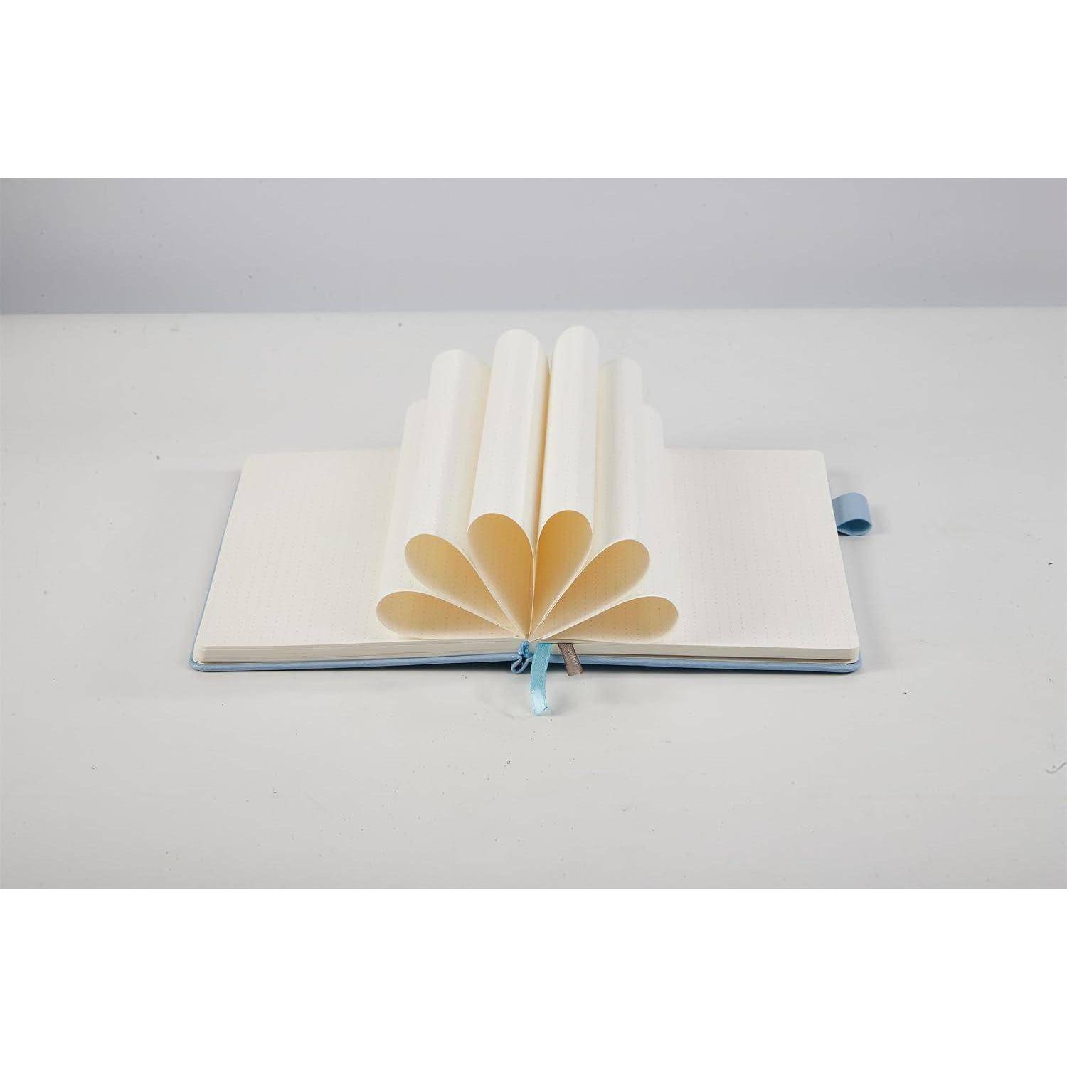 Offenes Notizbuch mit zu einer Blumenform gefalteten Seiten auf einer weißen Oberfläche, das eine dekorative Papierplastik schafft.