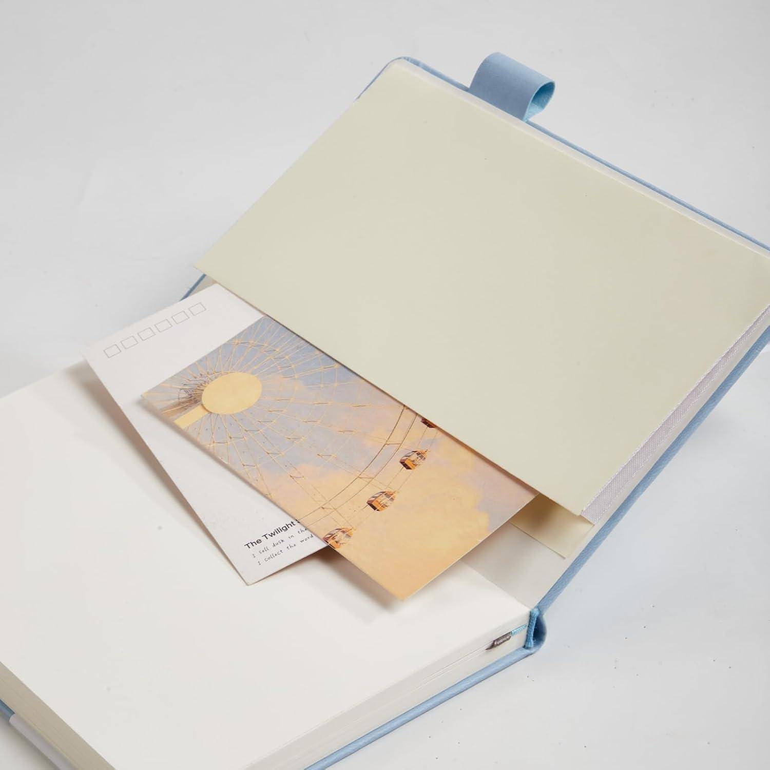 Offenes Buch oder Album mit hellem blauen Umschlag und leerem cremefarbenem Einleger, das zwei teilweise sichtbare bedruckte Karten oder Fotos enthält.