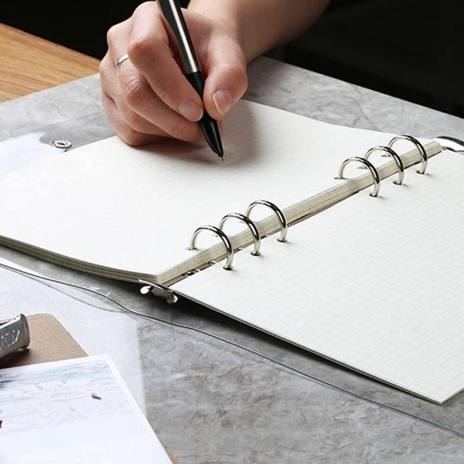 Eine Hand, die einen Stift über einem offenen Spiralblock auf einem Schreibtisch hält, bereit zu schreiben.