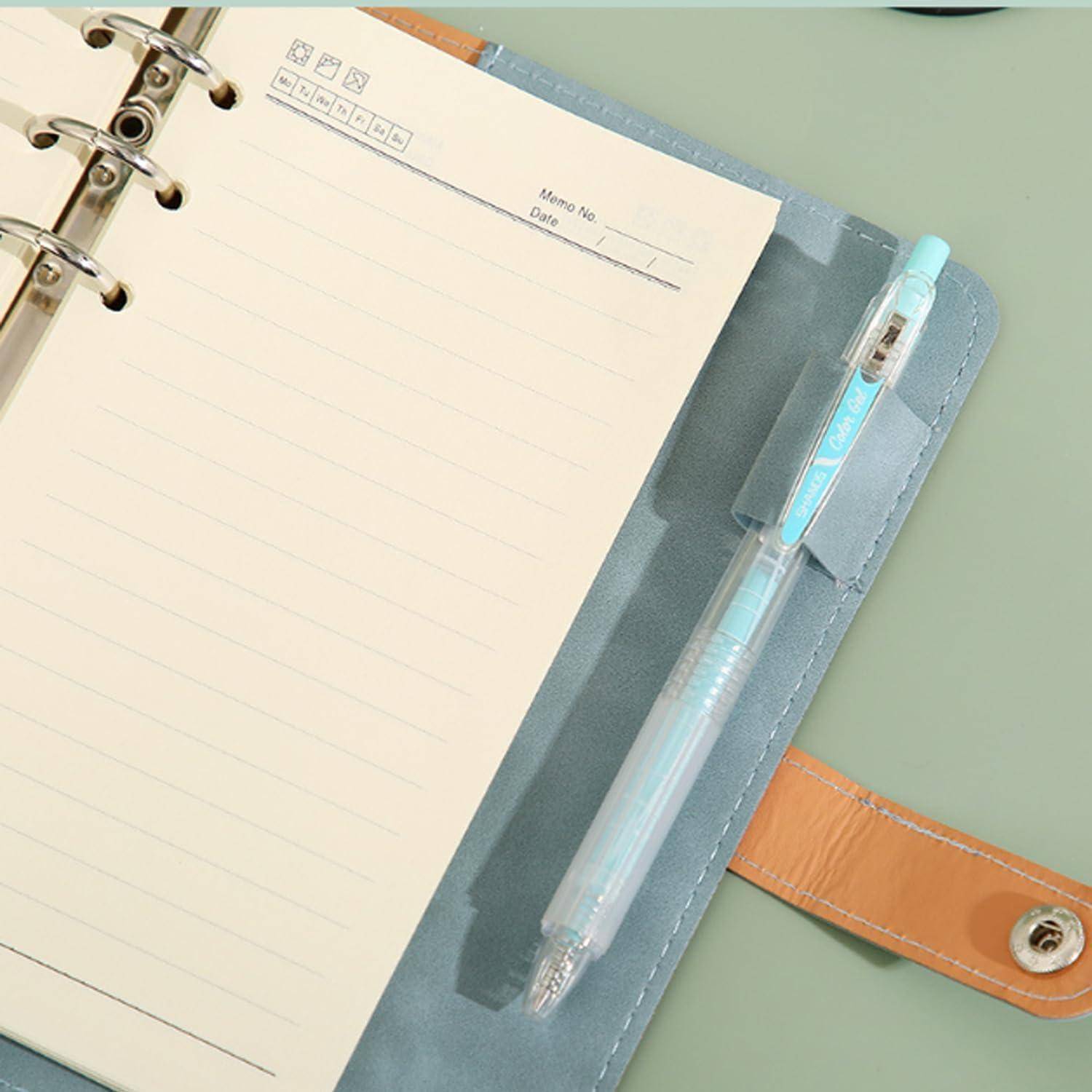 Offener ringgebundener Planer mit linierter Notizseite, Stift in der Seitentasche und beige Druckknopfverschluss auf mintgrünem Hintergrund.