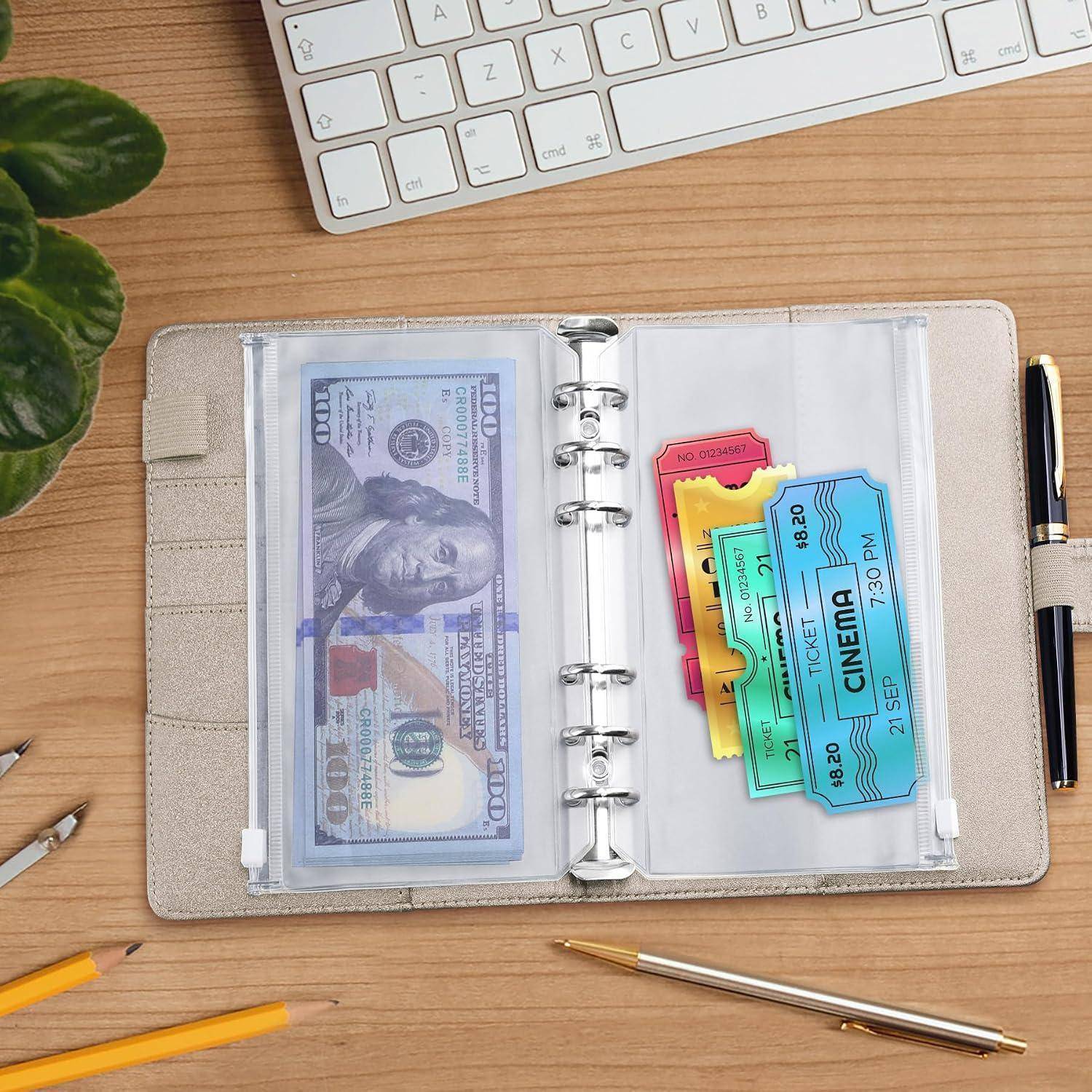 Offener Planer auf einem Schreibtisch mit einem 100-Dollar-Schein und bunten Kinokarten, daneben eine Tastatur, ein Stift und eine Pflanze.