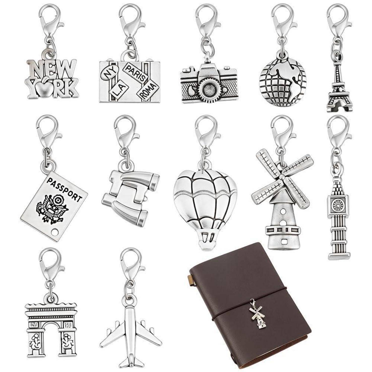 Sortierte, reisethematische Metallanhänger für Taschen und ein braunes Ledernotizuch, einschließlich Wahrzeichen, Kamera, Pass, Flugzeug, Windmühle und Heißluftballon.