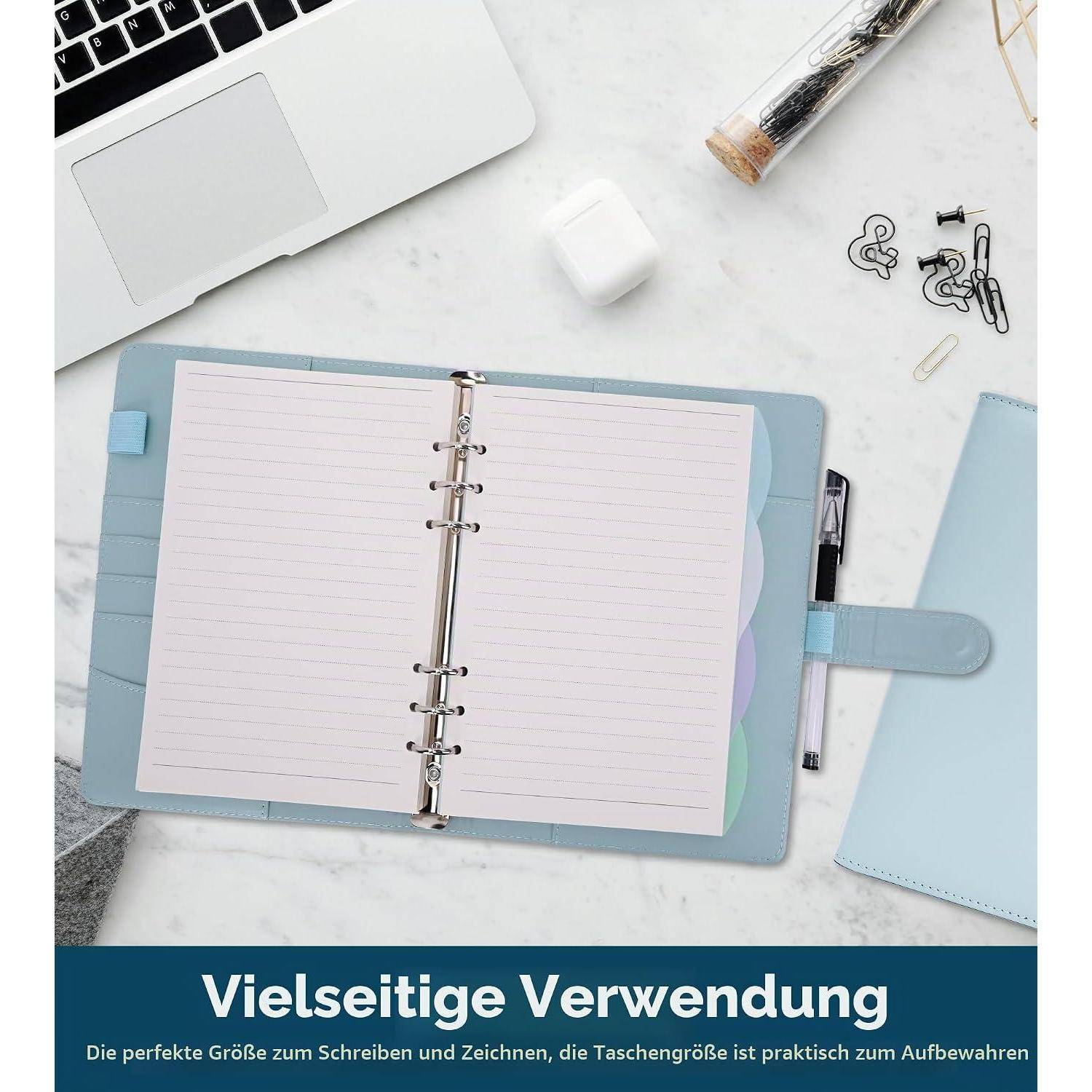 Schreibtischanordnung mit offenem Ringnotizuch, Stift, Laptopecke, Büroklammern und Radiergummi; deutscher Text liest sich als 