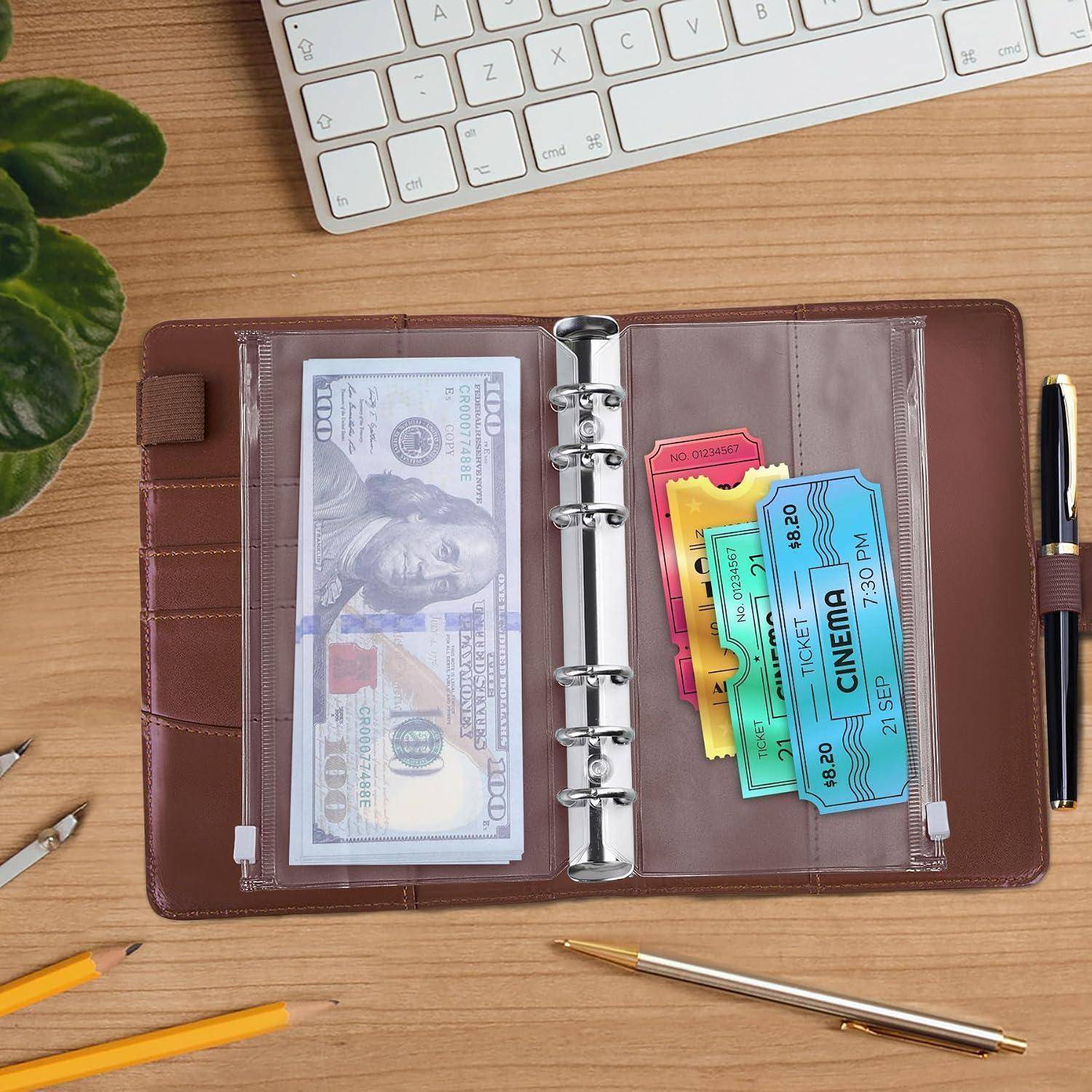 Offener brauner Ordner auf dem Schreibtisch mit Bargeld in einer Tasche und bunten Kinokarten in der anderen, mit einem Stift und einer Tastatur in der Nähe.