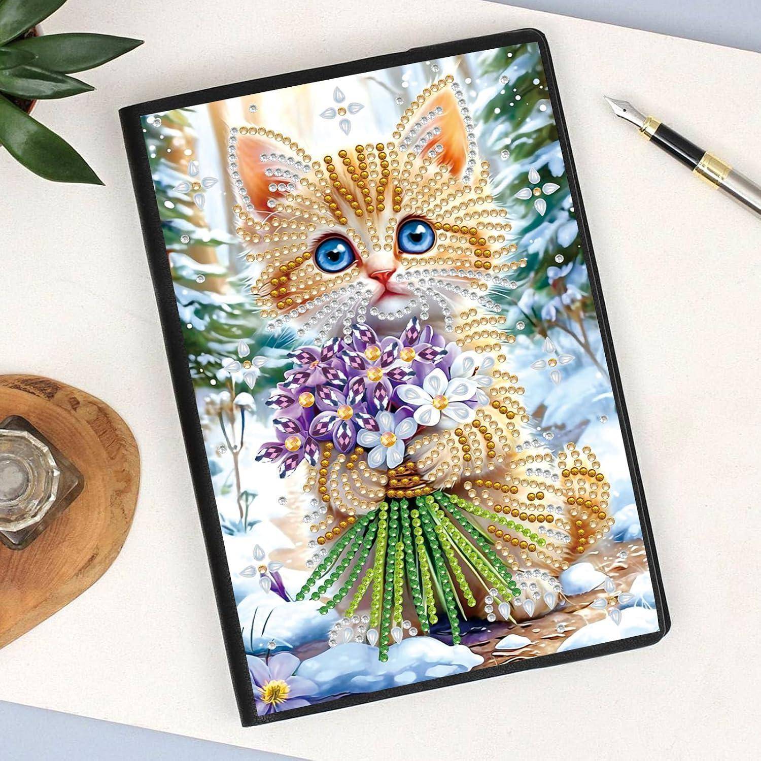 Dekoratives Bild einer mit Diamanten bemalten Katze, die lila und weiße Blumen hält, in einem schwarzen Rahmen auf einem Schreibtisch mit einem Stift und einer Pflanze in der Nähe gezeigt.