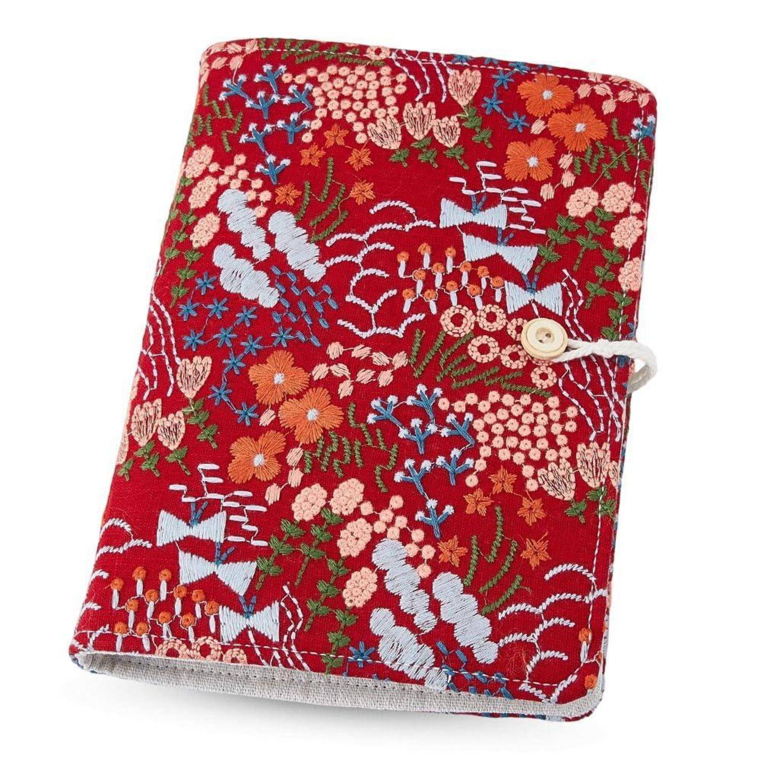 Rotes besticktes Stoffnotizbuch-Cover mit floralen und Vogel-Mustern, geschlossen mit einer Knopfschlaufe auf weißem Hintergrund.