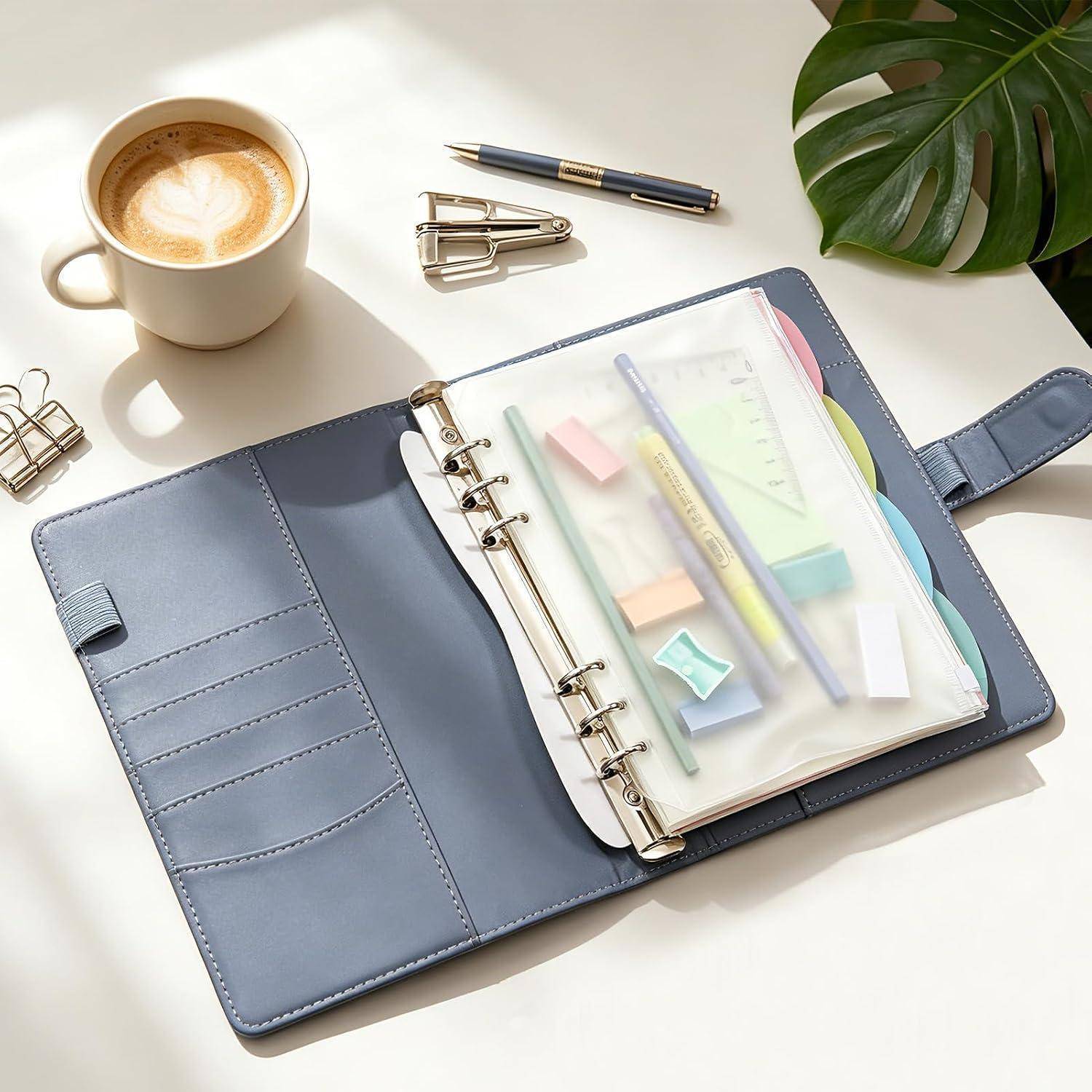 Offener blauer Ringordner-Planer auf einem Schreibtisch mit Stift, Kaffee, Locher und Pflanze, der organisierte Büromaterialien in einem hellen Arbeitsbereich zeigt.