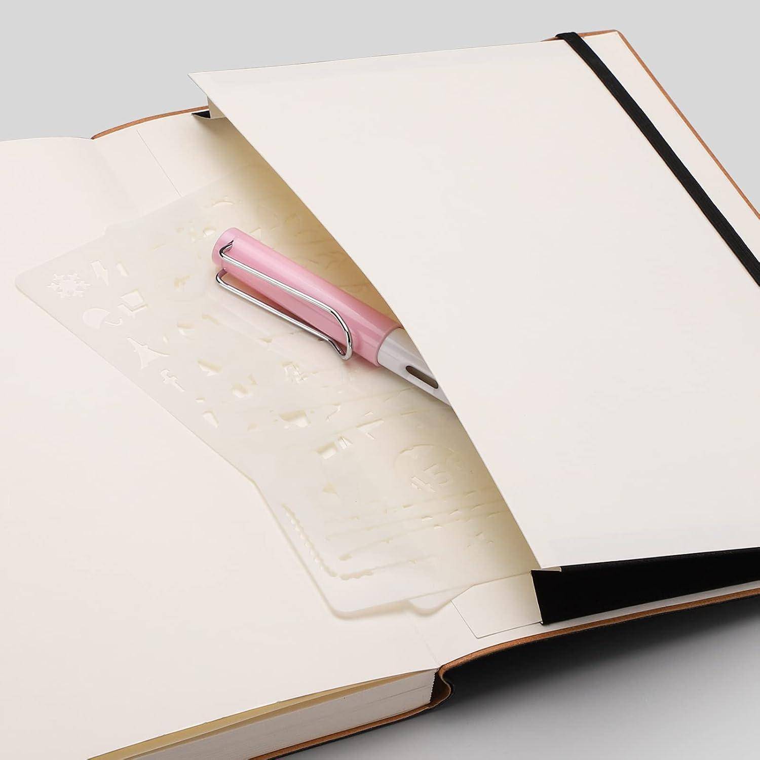 Rosa Stift ruht in einem offenen leeren Notizbuch, unter dem eine durchscheinende geprägte Seiteneinfügung sichtbar ist.