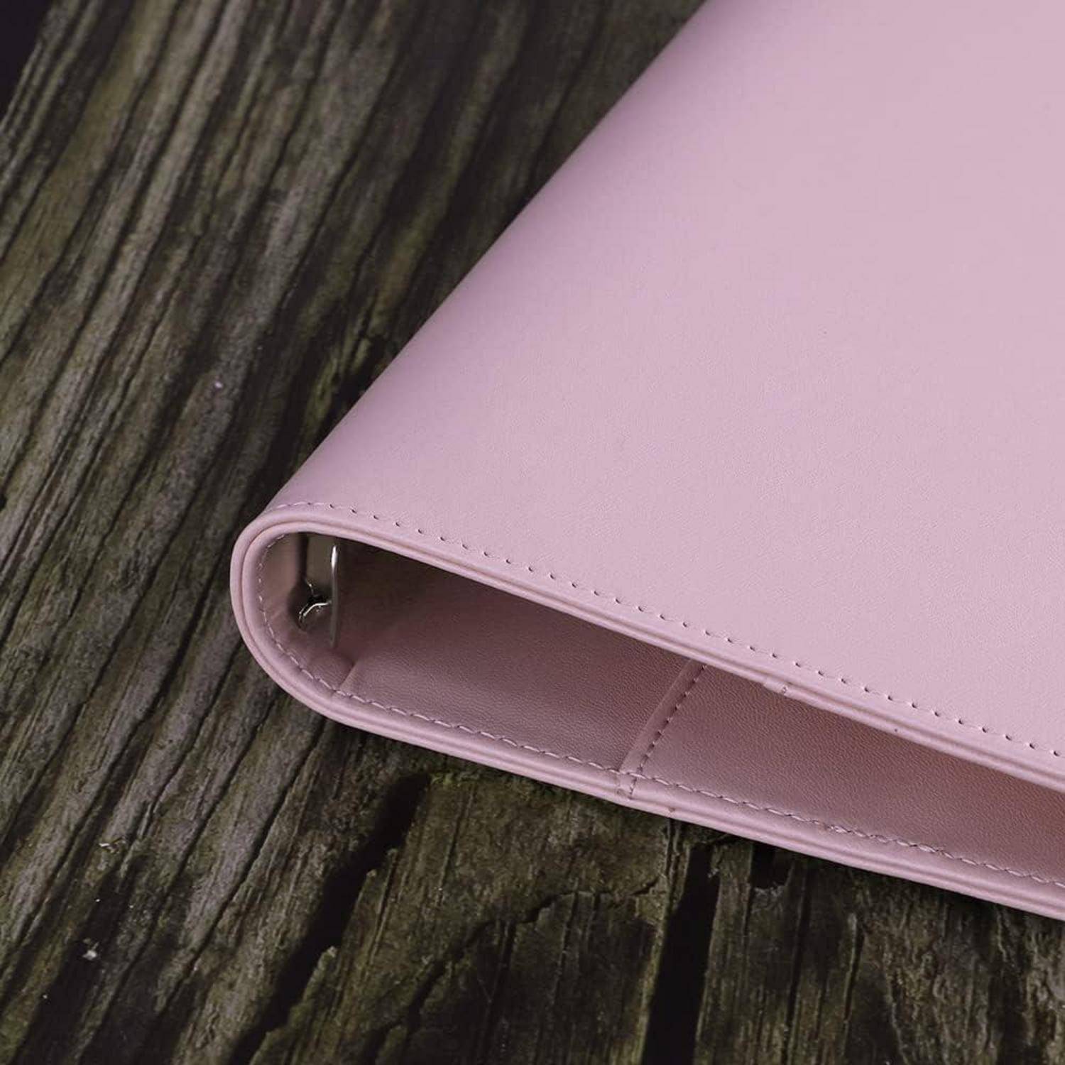 Nahaufnahme eines hellrosa Leder-Ordners oder einer Clutch auf einer verwitterten Holzoberfläche.