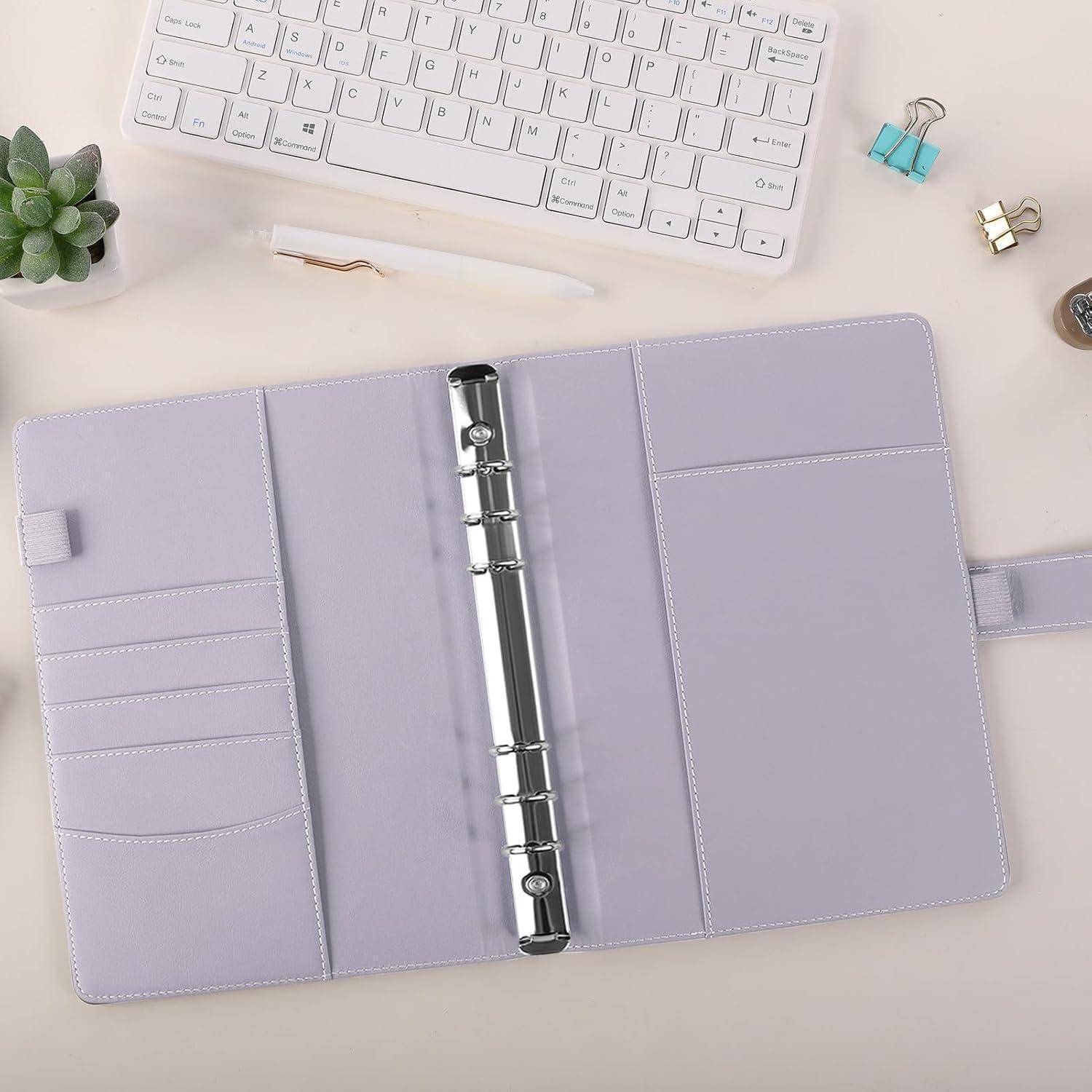 Offener Lavendelring-Ordner-Planer mit mehreren Kartensteckplätzen und Taschen auf einem Schreibtisch unter einer Tastatur und einem Stift, mit kleinen Klammern und einer Pflanze in der Nähe.