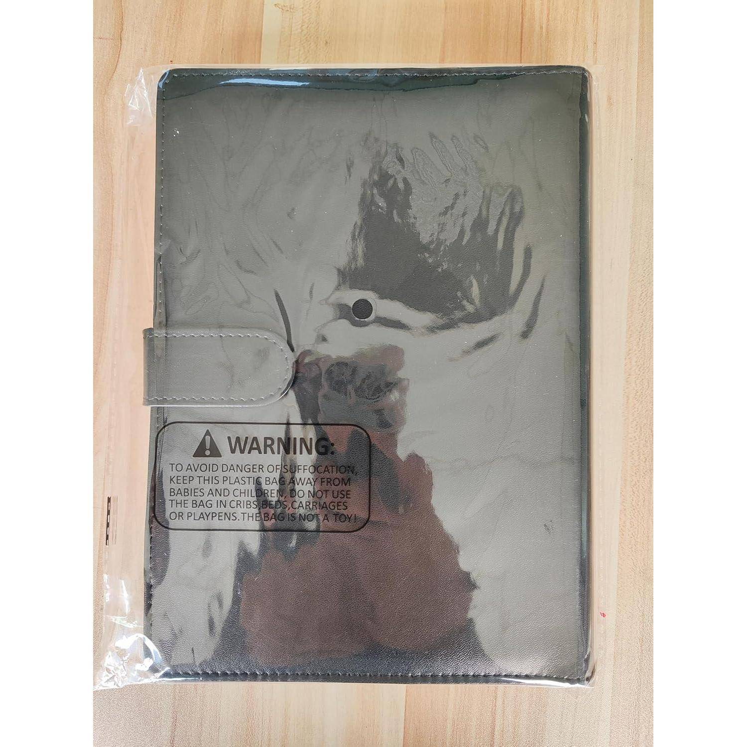 Ein reflektierendes silbernes Tablet oder Notizbuch-Cover in einer transparenten Plastikfolie, mit einem Riemenverschluss und einem Warnschild darauf, die Tasche von Babys und Kindern fernzuhalten.