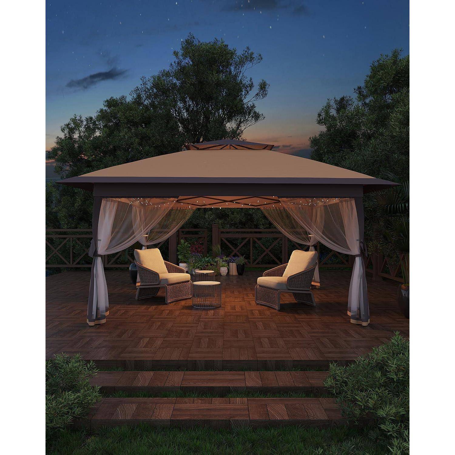 Gartenlaube mit Lounge-Bereich bei der Dämmerung mit zwei Sesseln, durchsichtigen Vorhängen und einem kleinen Tisch auf einer Holzterrasse, umgeben von Bäumen.
