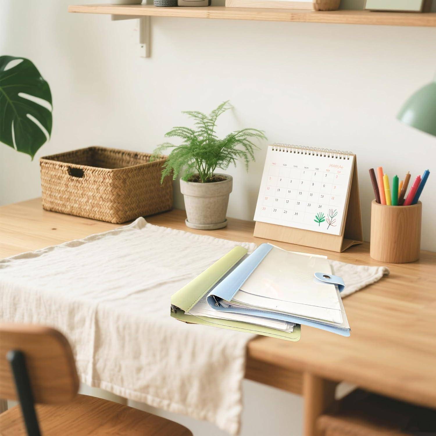 Ein ordentlicher Arbeitstisch im Homeoffice mit Notizbüchern, Stiften, einer kleinen Topfpflanze, einem Kalender und einem Aufbewahrungskorb in einem minimalistischen Arbeitsbereich.