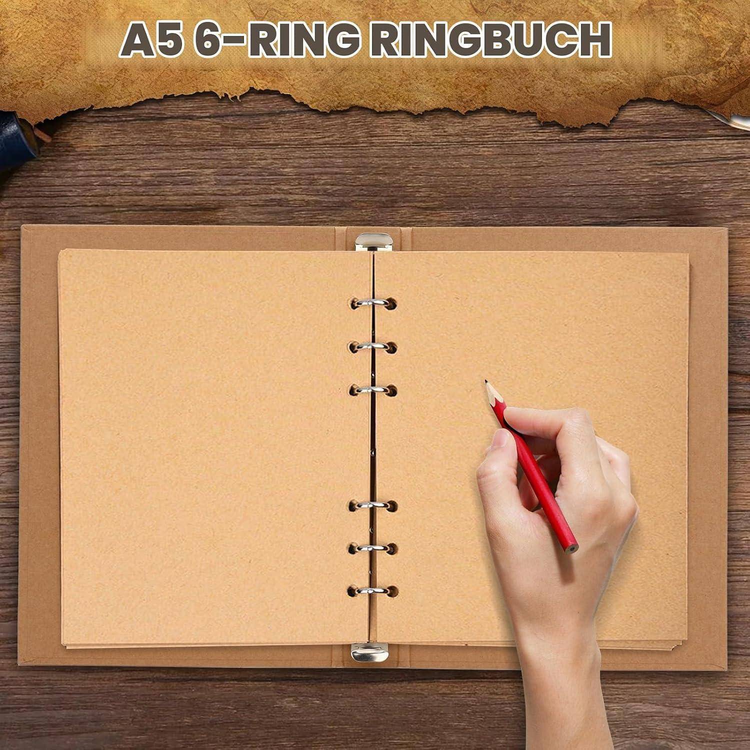 Offenes A5 6-Ring Ringbuch auf einem Holzschreibtisch, mit einer Hand, die einen roten Bleistift über der leeren Seite hält, und dem Text „A5 6-RING RINGBUCH