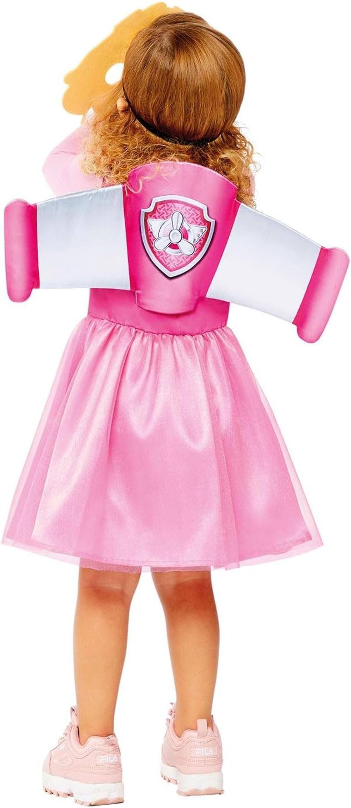 Rückansicht eines Kindes, das ein rosa Rock-Kostüm von „Paw Patrol" Skye mit Flügeln und Turnschuhen trägt und eine Spielfigur über dem Kopf hält.
