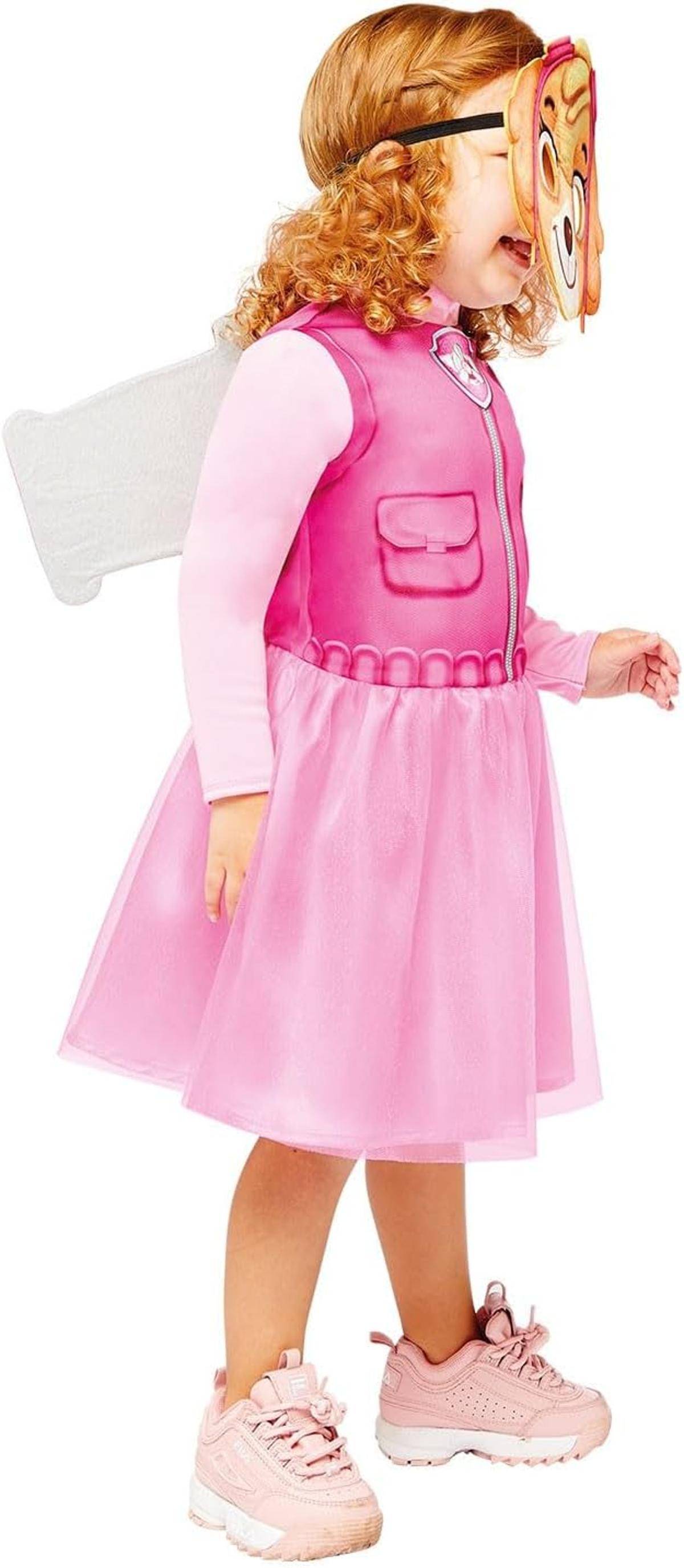 Junges Mädchen in einem rosa Kleid und Sneakern, das eine Cartoon-Maske trägt und weiße Flügel trägt, gekleidet wie eine Fee oder Kostümcharakter.