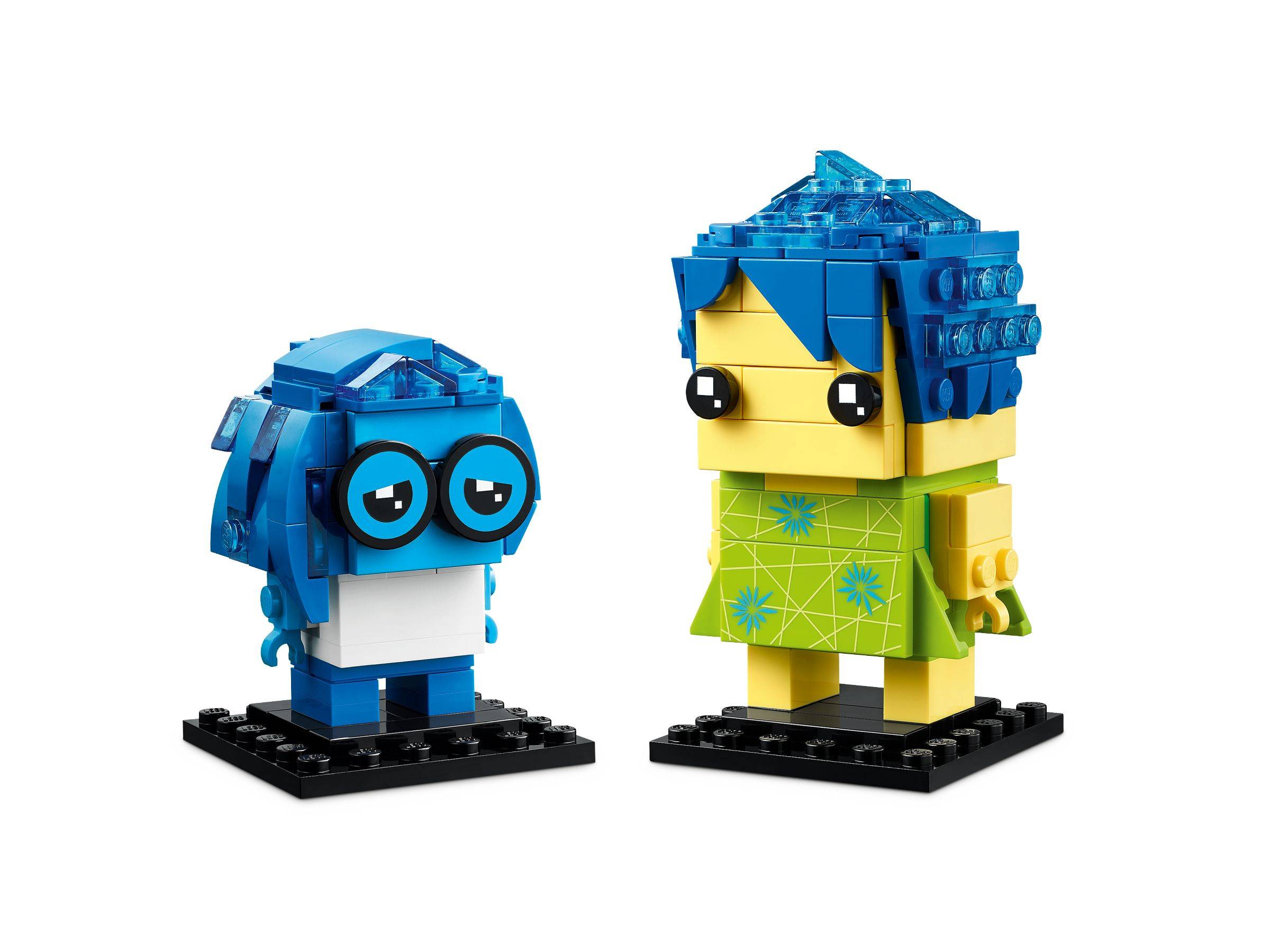 Zwei LEGO-ähnliche Cartoon-Figuren mit blauen Haaren, eine kleine und rundliche mit Brille und eine größere in einem grünen Kleid, stehend auf schwarzen Sockeln.