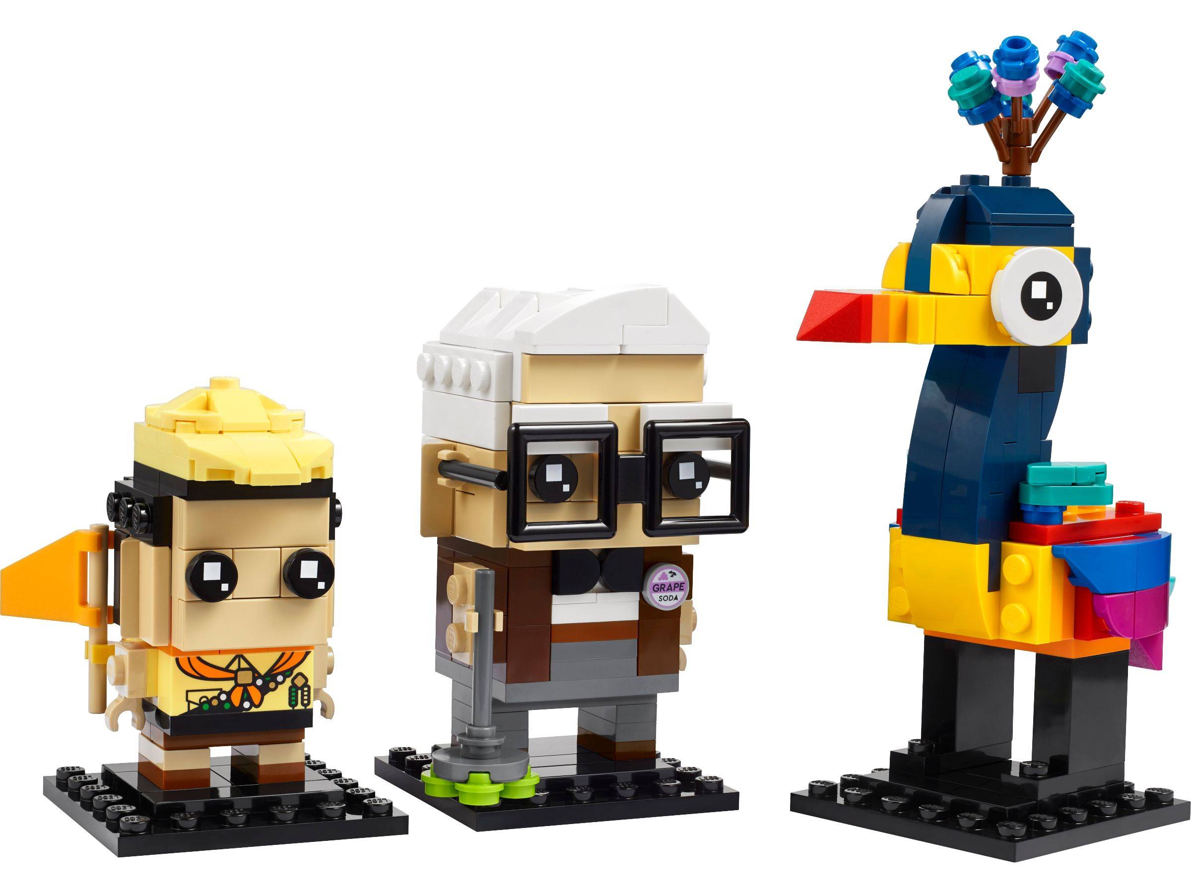 Drei LEGO-ähnliche Vogelfiguren auf schwarzen Sockeln: eine kleine blonde Figur, eine bespectacelte ältere Figur und ein großer bunter Vogel mit großem Schnabel und blumenähnlichem Kopfschmuck.