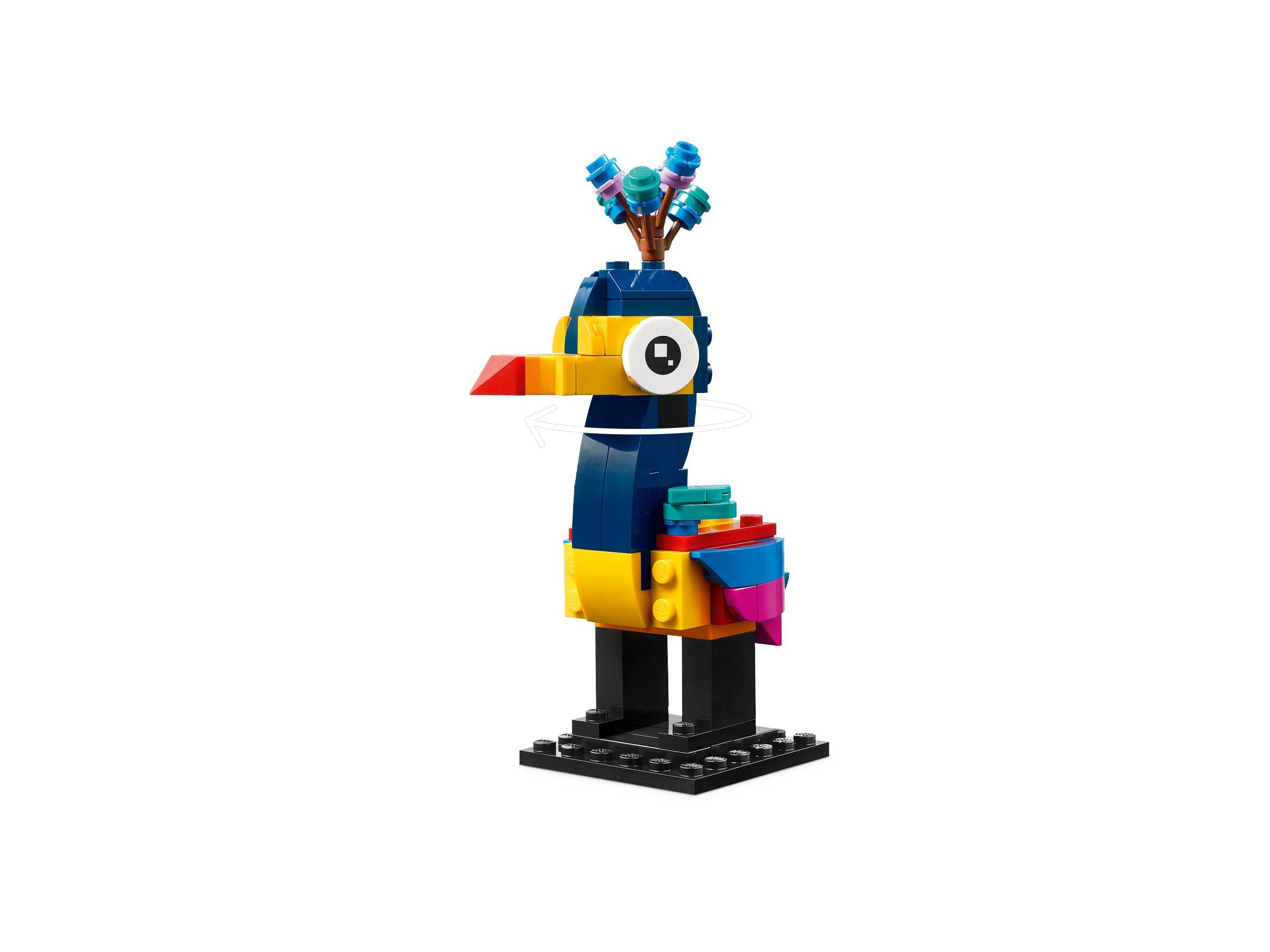 Eine bunte LEGO-ähnliche Vogelfigur mit einem langen Schnabel, einem Auge und einer blumenartigen Haube, die auf einem schwarzen Sockel vor weißem Hintergrund steht.