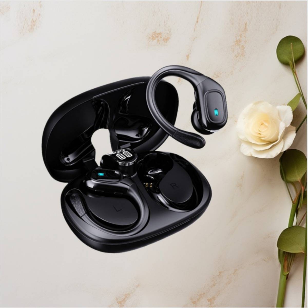 Schwarze kabellose Open-Ear-Ohrhörer in einem Ladeetui, angezeigt auf einer hellen Marmoroberfläche neben einer weißen Rose und grünen Blättern.