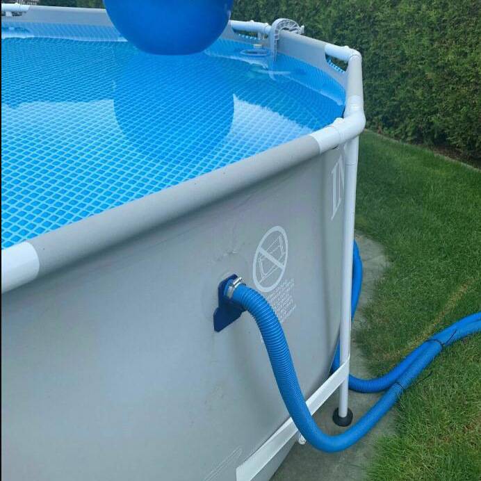 Aufstellpool mit blauem Wasser und einem blauen Schlauch an der Seite angebracht, gezeigt neben einem Rasenplatz und einer Hecke.