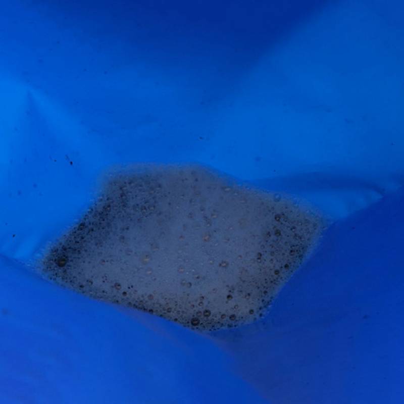 Schaumige graue Flüssigkeit sammelte sich am Boden eines leuchtend blauen Kunststoffbehälters oder einer leuchtend blauen Kunststofftasche.