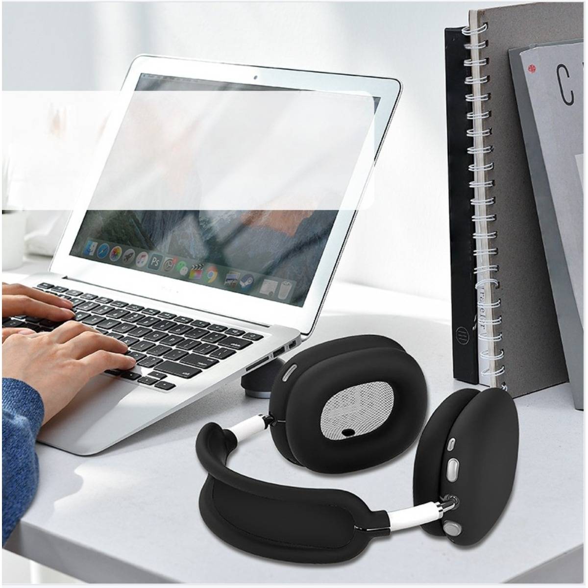 Schwarze Over-Ear-Kopfhörer auf einem Schreibtisch neben einem Laptop, während jemand tippt, zeigt ein Homeoffice-Setup.