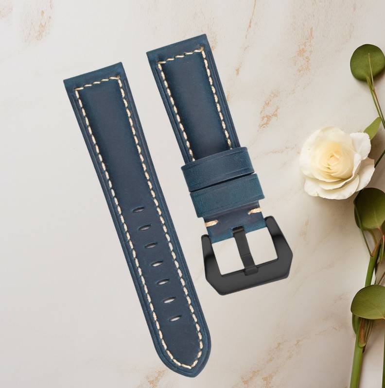 Zwei blaue Lederwatchbänder mit weißer Naht und schwarzen Schnallen, gezeigt auf einer hellen Marmoroberfläche mit einer weißen Blume.