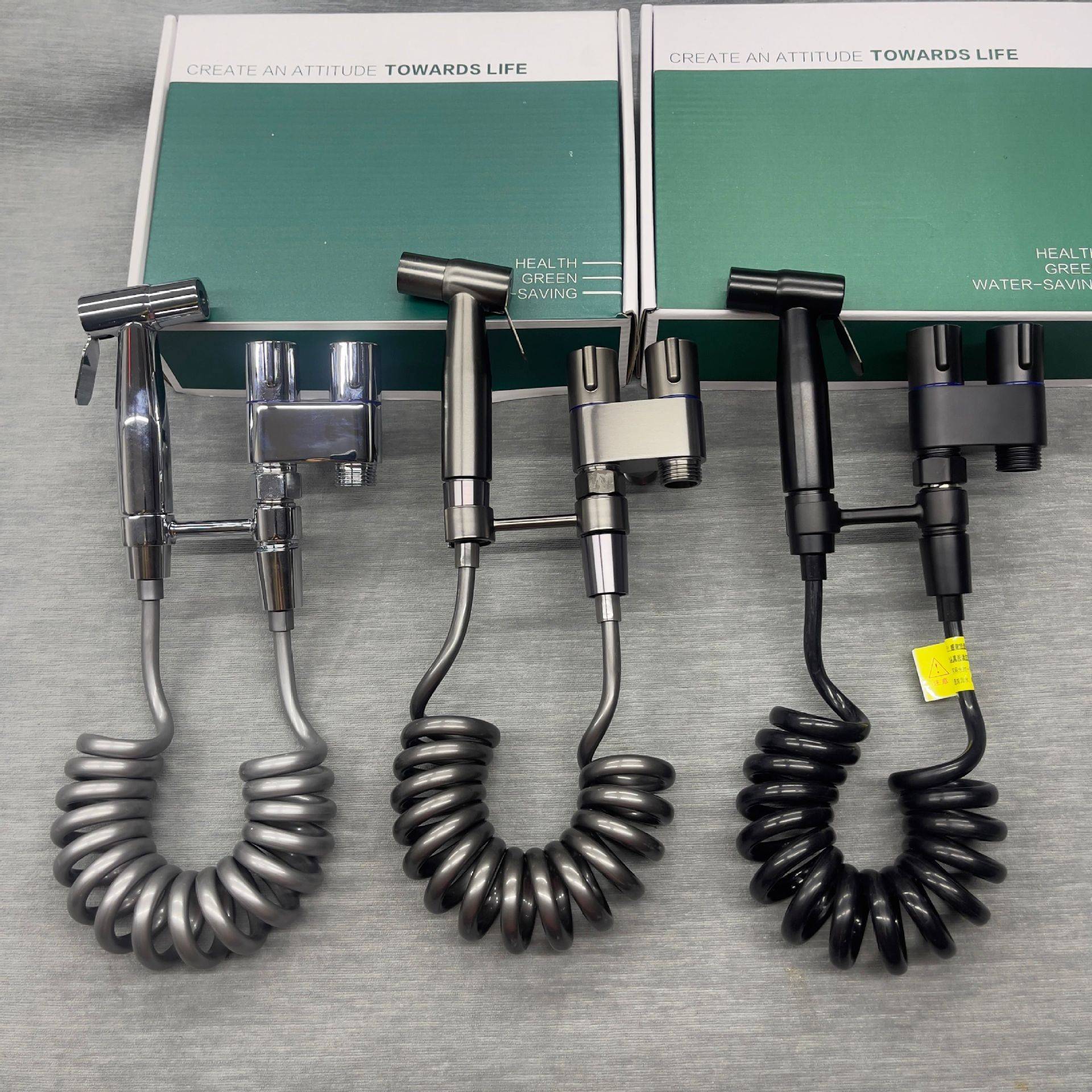 Sechs tragbare Bidet-Sprayer auf der Verpackung ausgestellt, mit Chrom-, Silber- und schwarzen Oberflächen mit Spiralschläuchen und Text „gesundheitlich grünes Wassersparen