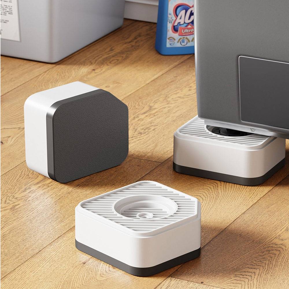 Drei kleine quadratische weiß-graue Geräte auf einem Holzboden, eines unterstützt einen Monitorständer und eines ist in der Nähe positioniert.