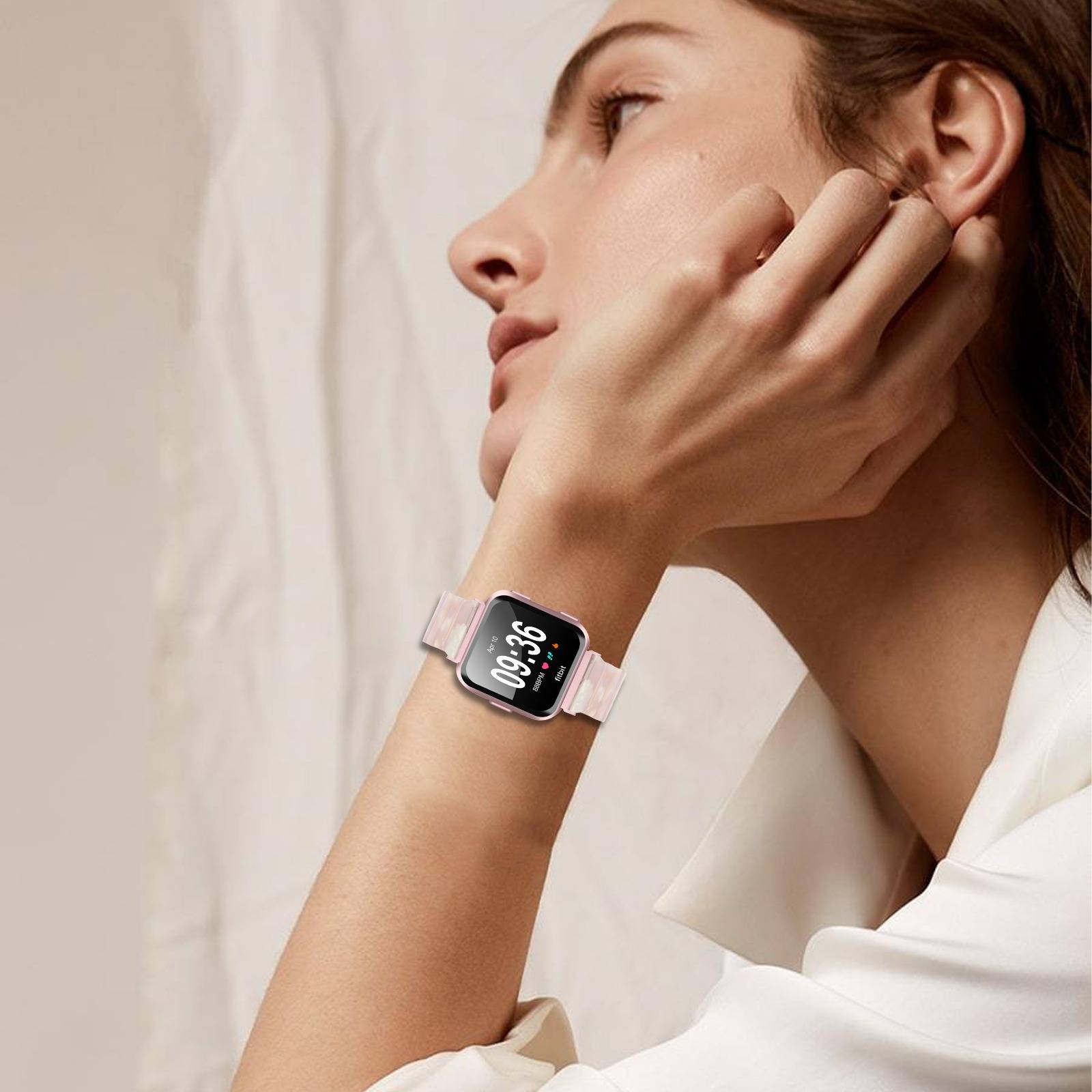 Frau im Profil, die eine rosa Smartwatch trägt, mit ihrer Hand auf ihrem Gesicht ruhend vor einem weichen neutralen Hintergrund.