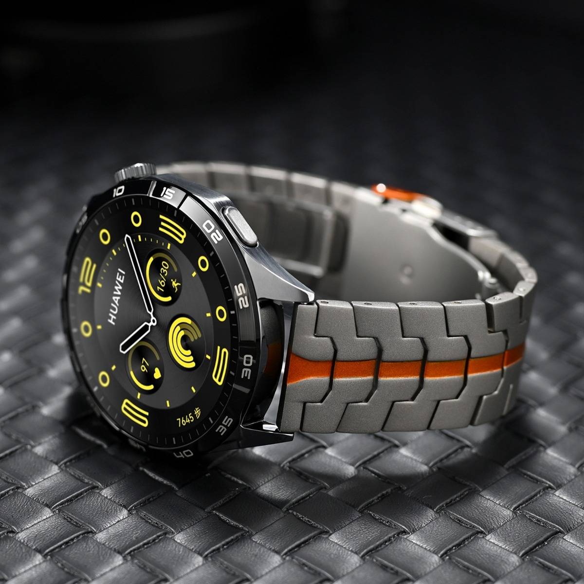 Eine Huawei-Smartwatch mit schwarzem rundem Zifferblatt und grauem Metallband, akzentuiert durch einen orangefarbenen Streifen, gezeigt auf einer dunkel strukturierten Oberfläche.