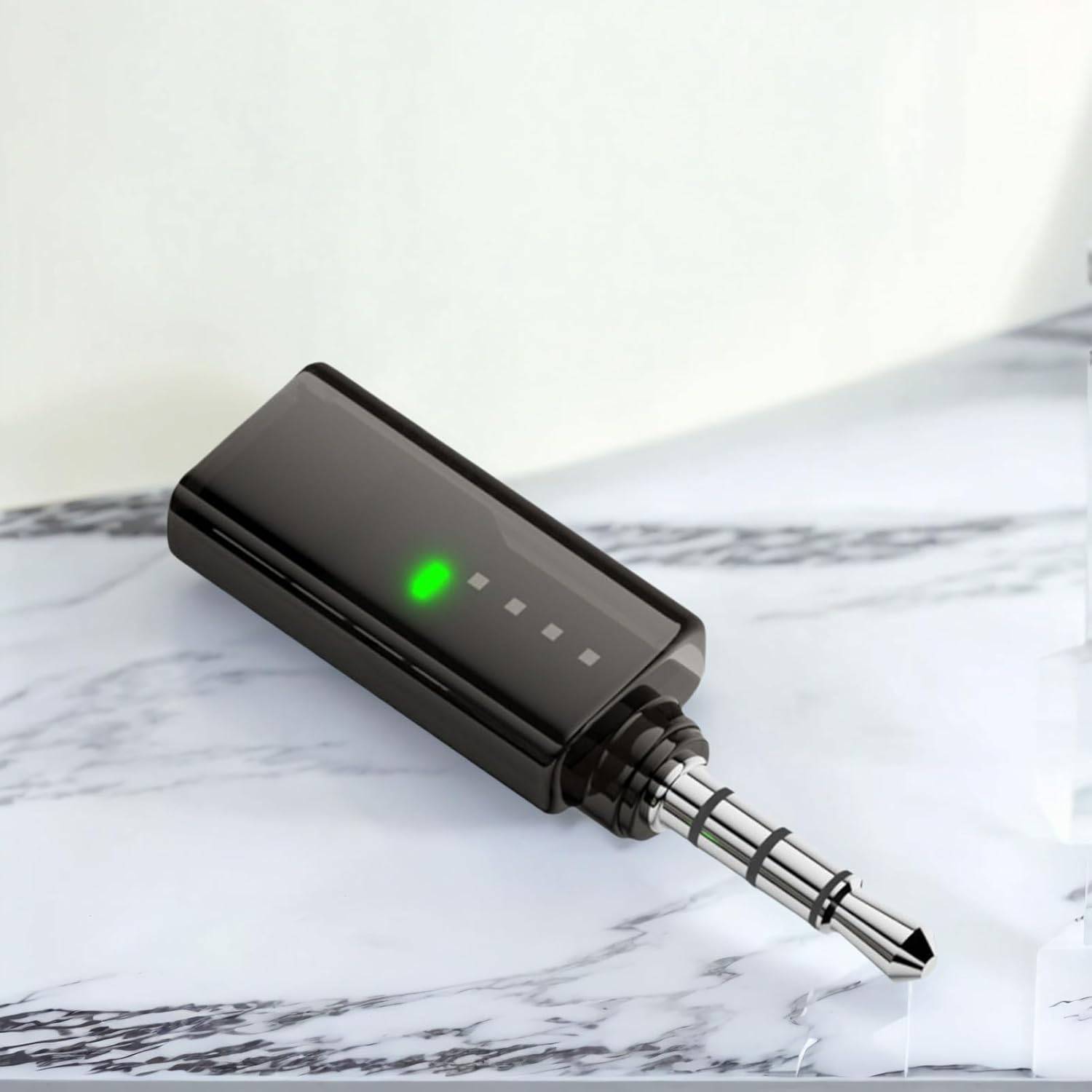 Schwarzer kabelloser Mikrofonsender mit grüner LED und Batterieindikatoren, liegend auf einer Marmoroberfläche mit angeschlossenem Steckerverbinder.