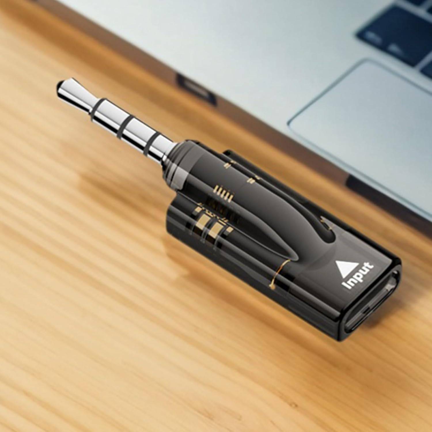 Schwarzer 3,5-mm-Audio-Steckeradapter auf einem Holzschreibtisch, beschriftet mit „Input