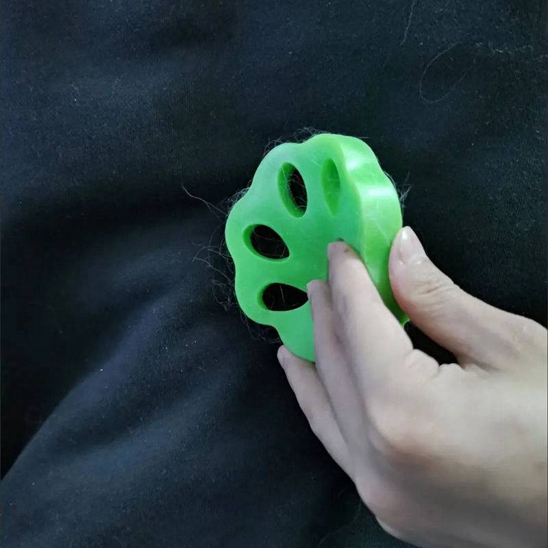 Eine Hand hält ein leuchtend grünes pfotensommes Spielzeug oder Stressabbau-Spielzeug gegen einen dunklen Stoffhintergrund.