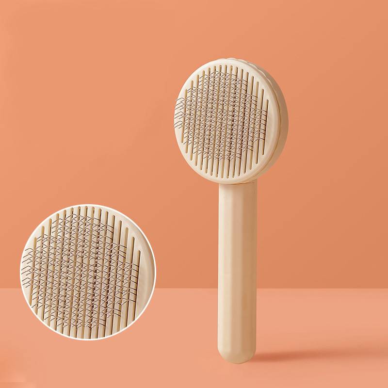 Beige-farbene Haustierbürste mit Metallborsten, von vorne und in Nahaufnahme auf pfirsichfarbenem Hintergrund gezeigt.