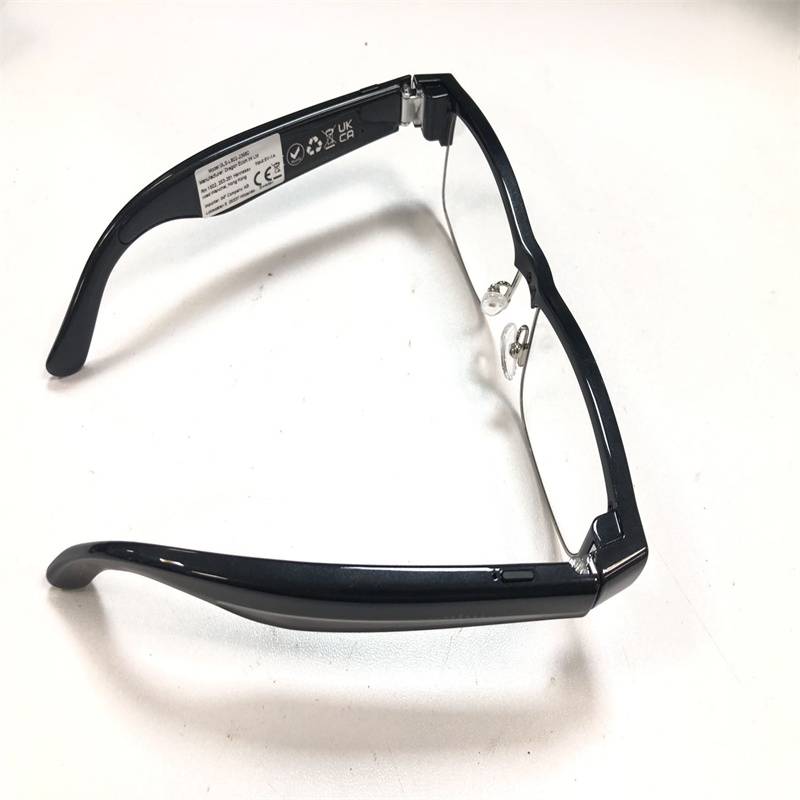 Schwarze rechteckige Brille mit klaren Gläsern und Seitenetiketten, gefaltet auf weißem Hintergrund dargestellt.