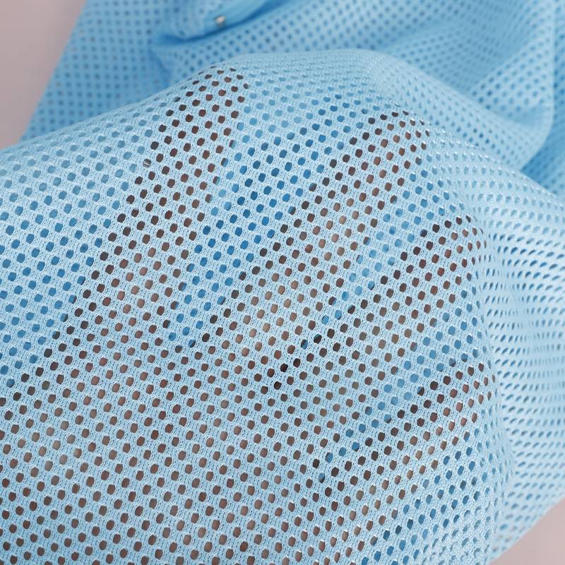 Nahaufnahme einer Person, die eine hellblaue Mesh-Gesichtsmaske trägt, die das strukturierte perforierte Gewebe und die Ohrschlaufen zeigt.