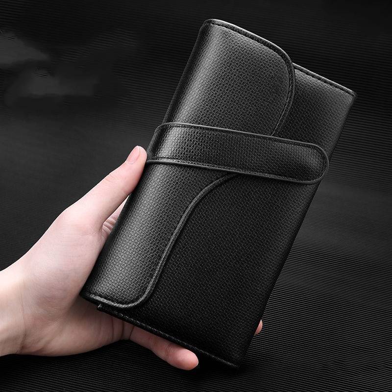 Hand hält eine schwarze strukturierte Lederbrieftasche mit umlaufendem Riemenverschluss.