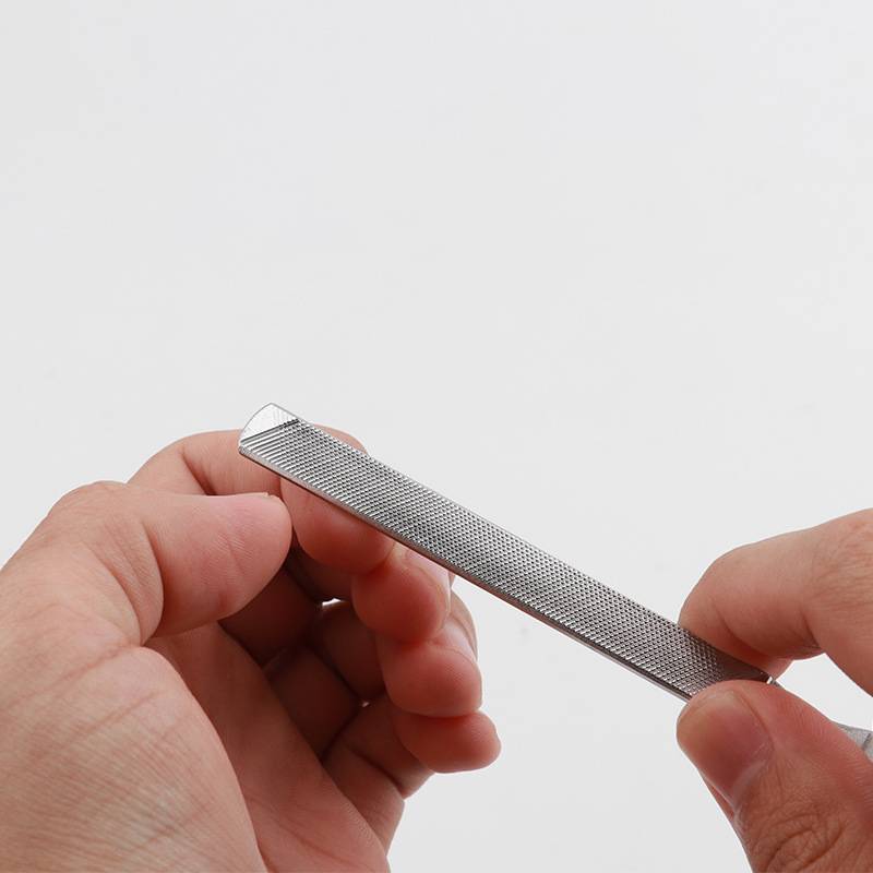 Nahaufnahme von Händen, die eine Metallnagelfeile halten und damit einen Fingernagel gegen einen einfachen weißen Hintergrund formen.