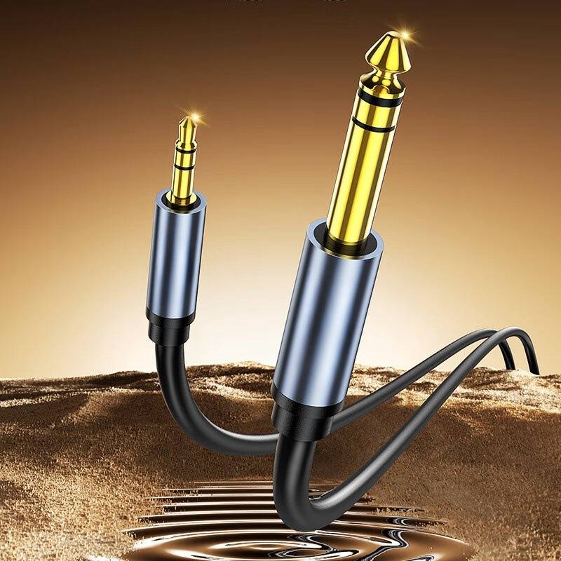 Zwei vergoldete 1/4-Zoll-Audiostecker, die durch ein schwarzes Y-förmiges Kabel verbunden sind, dargestellt als Produktbild auf einem warmen braunen Hintergrund.