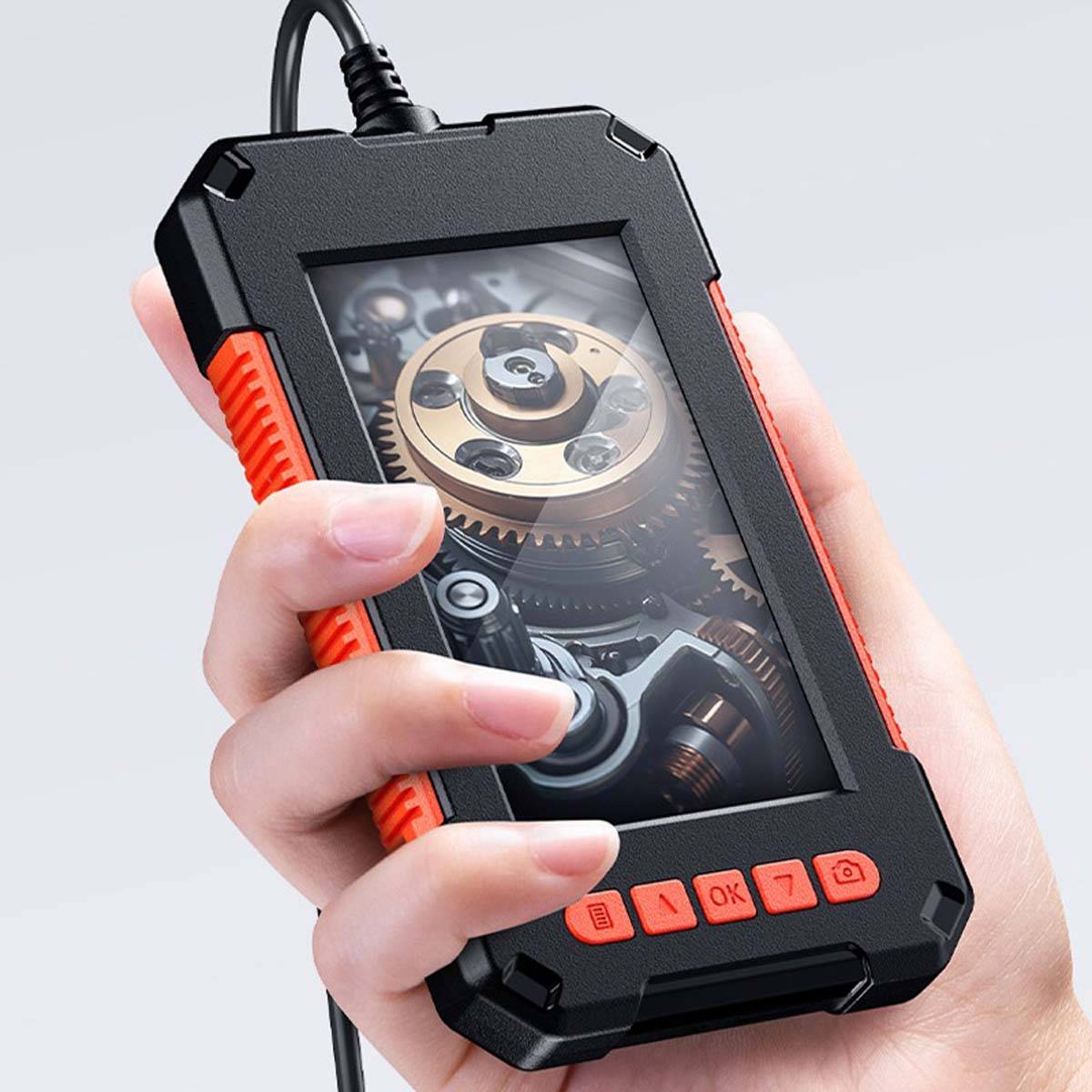 Eine Hand hält ein robustes tragbares Inspektionsgerät mit einem klaren Fenster, das Zahnräder und innere Mechanismen zeigt, mit orangefarbenen Steuertasten.