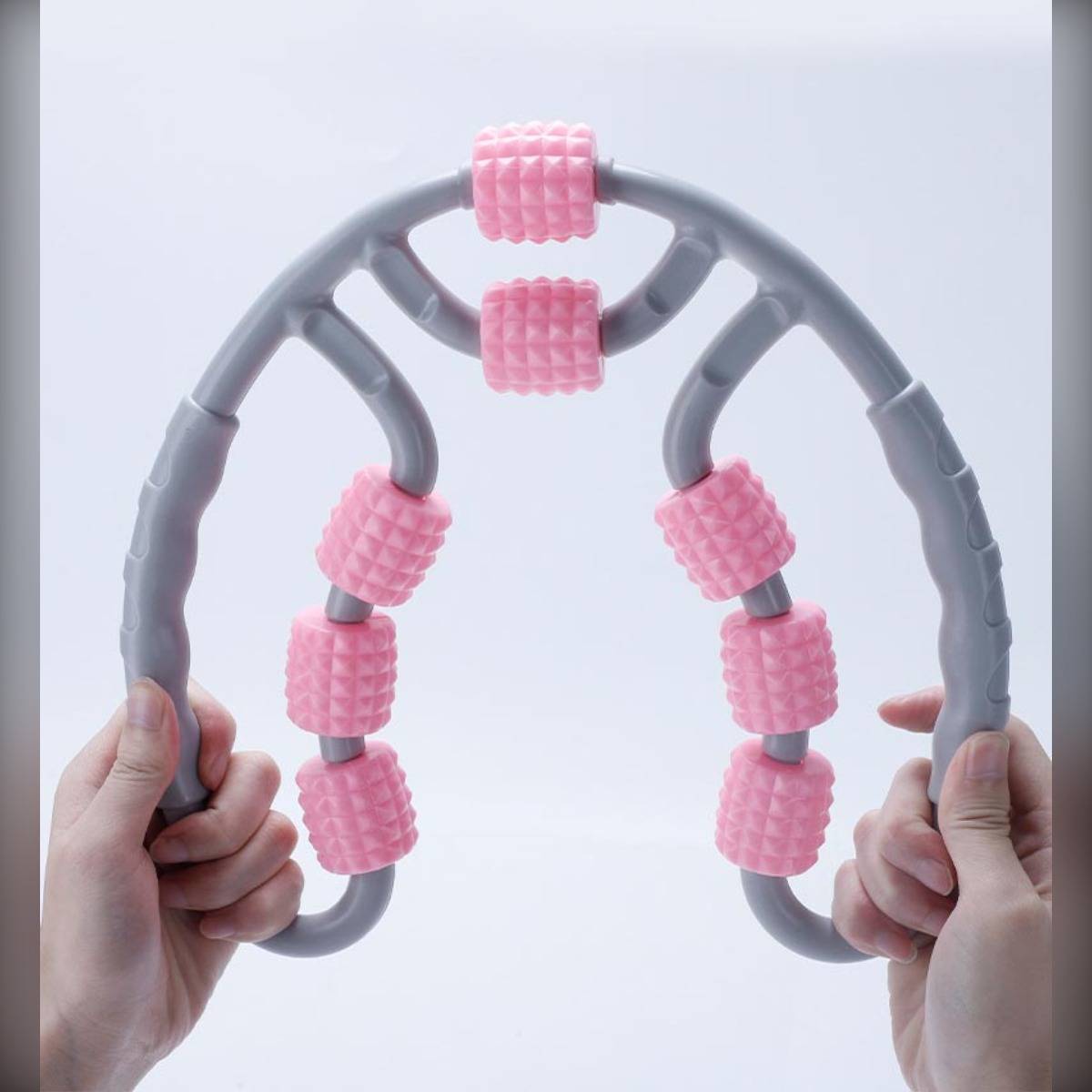 Hände halten einen grauen Rückendehner mit rosa Schaumstoffrollen, die ein flexibles Massage-/Trainingsgerät auf weißem Hintergrund zeigen.