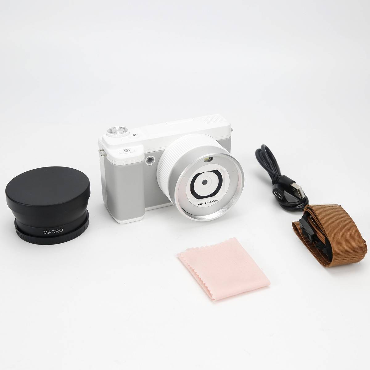 Weiße kompakte Kamera mit großem Objektiv, Makrovorsatz, USB-Kabel und brauner Schutztasche auf weißem Hintergrund arrangiert.