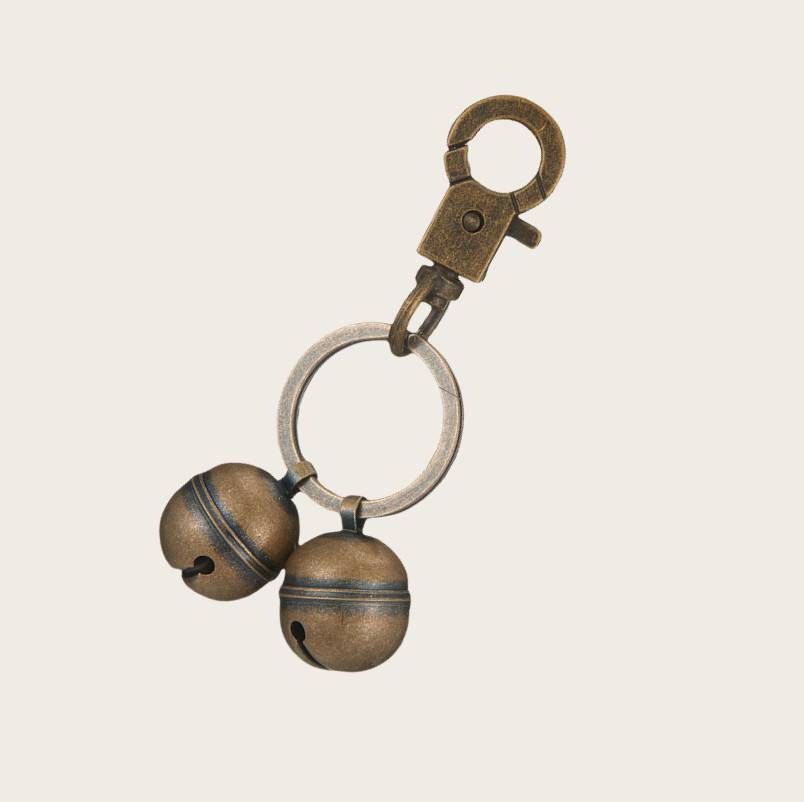 Schlüsselanhänger aus Bronzemetall mit Federklemme, Ring und zwei kleinen glockenförmigen Anhängern auf einfachem Hintergrund.