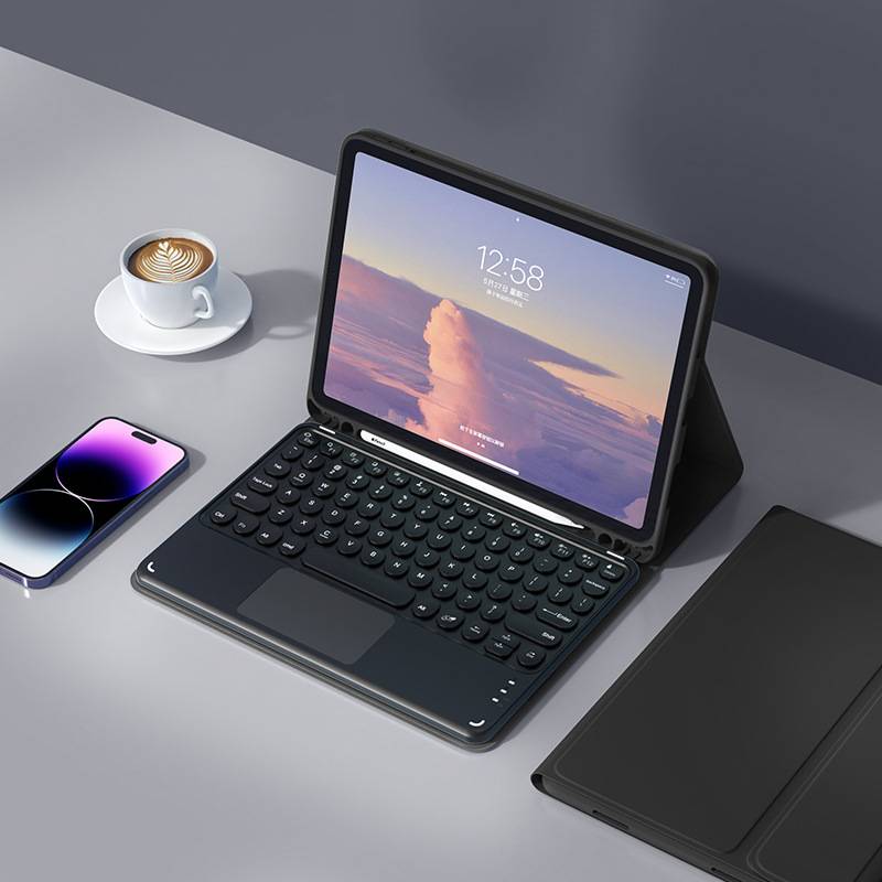 Ein Tablet in einer Tastaturhülle auf einem Schreibtisch neben einem Smartphone, einem Laptop und einer Tasse Kaffee, das einen Sperrbildschirm um 12:58 Uhr anzeigt.