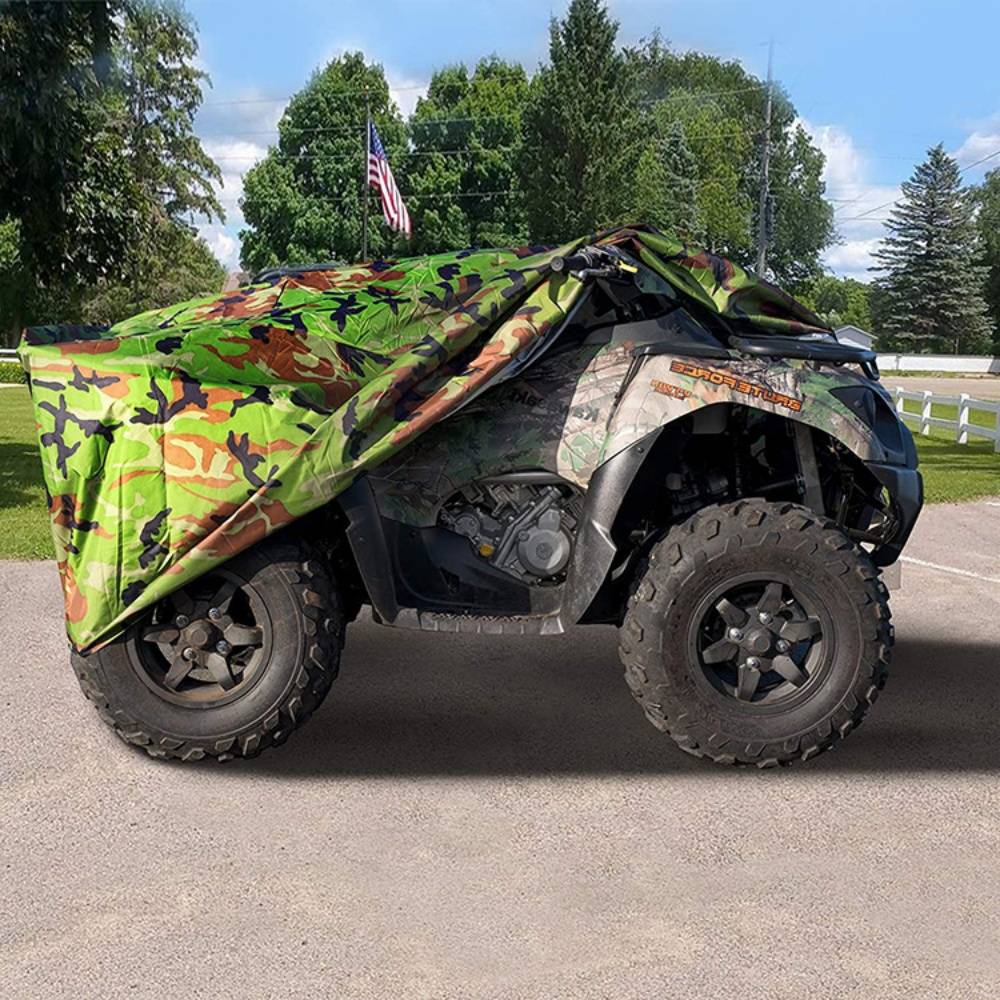 Getarnter Geländewagen mit ATV-Design auf Pflaster geparkt, bedeckt von einer grün-braunen Plane, mit einer amerikanischen Flagge und Bäumen im Hintergrund.